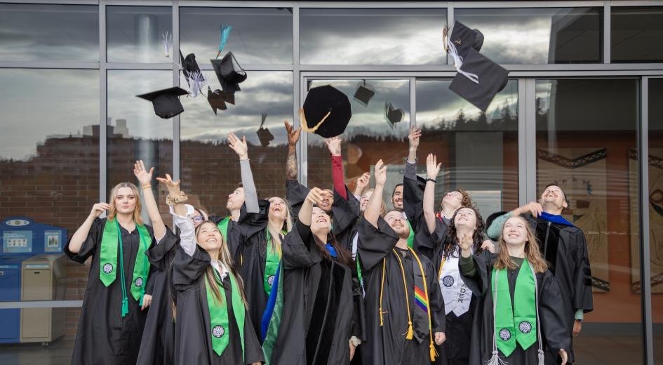 Graduates in black caps and gowns toss mortarboards into the air outdoors.