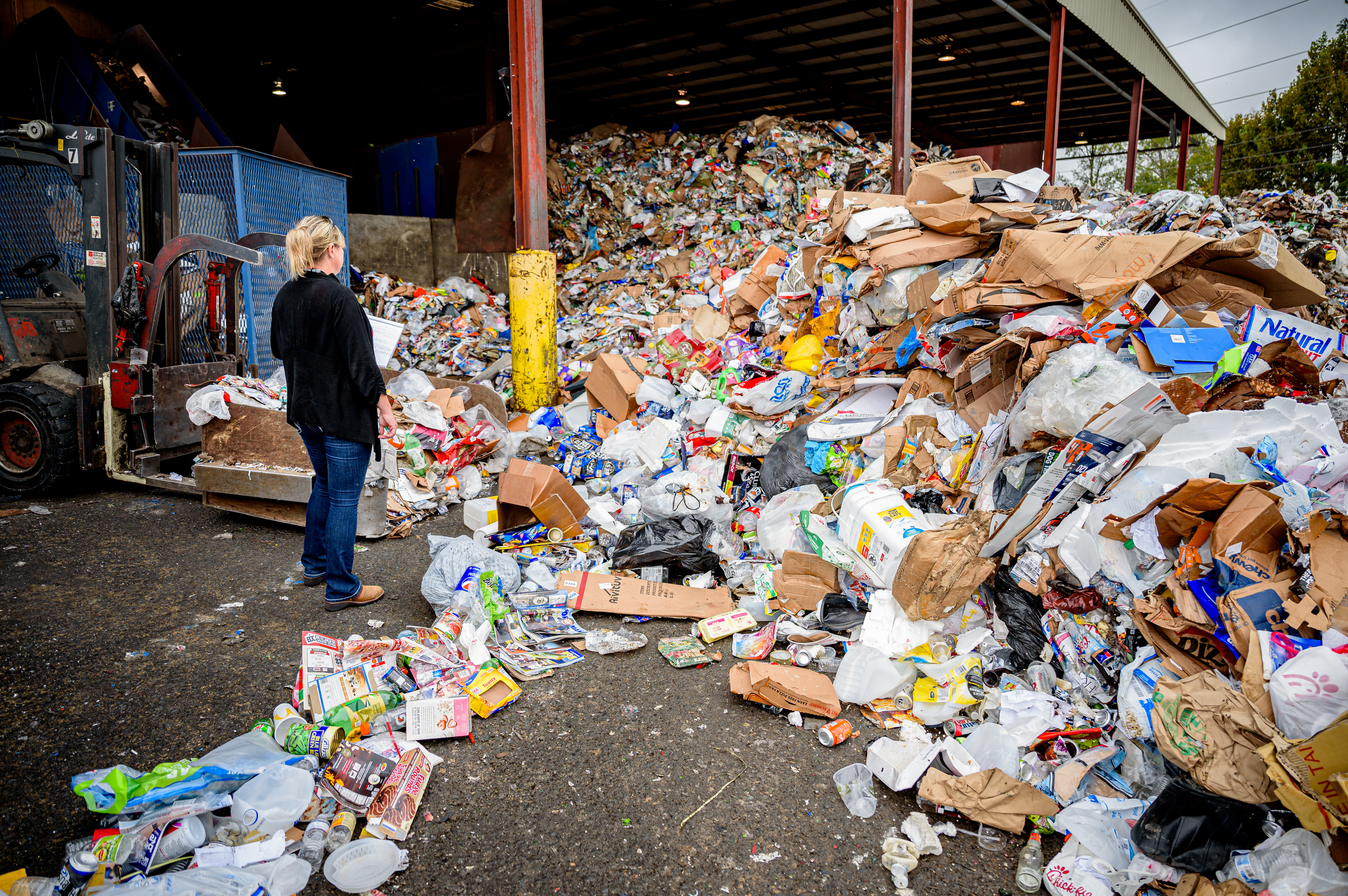 Person standing before a large pile of mixed recyclables at an industrial sorting facility.