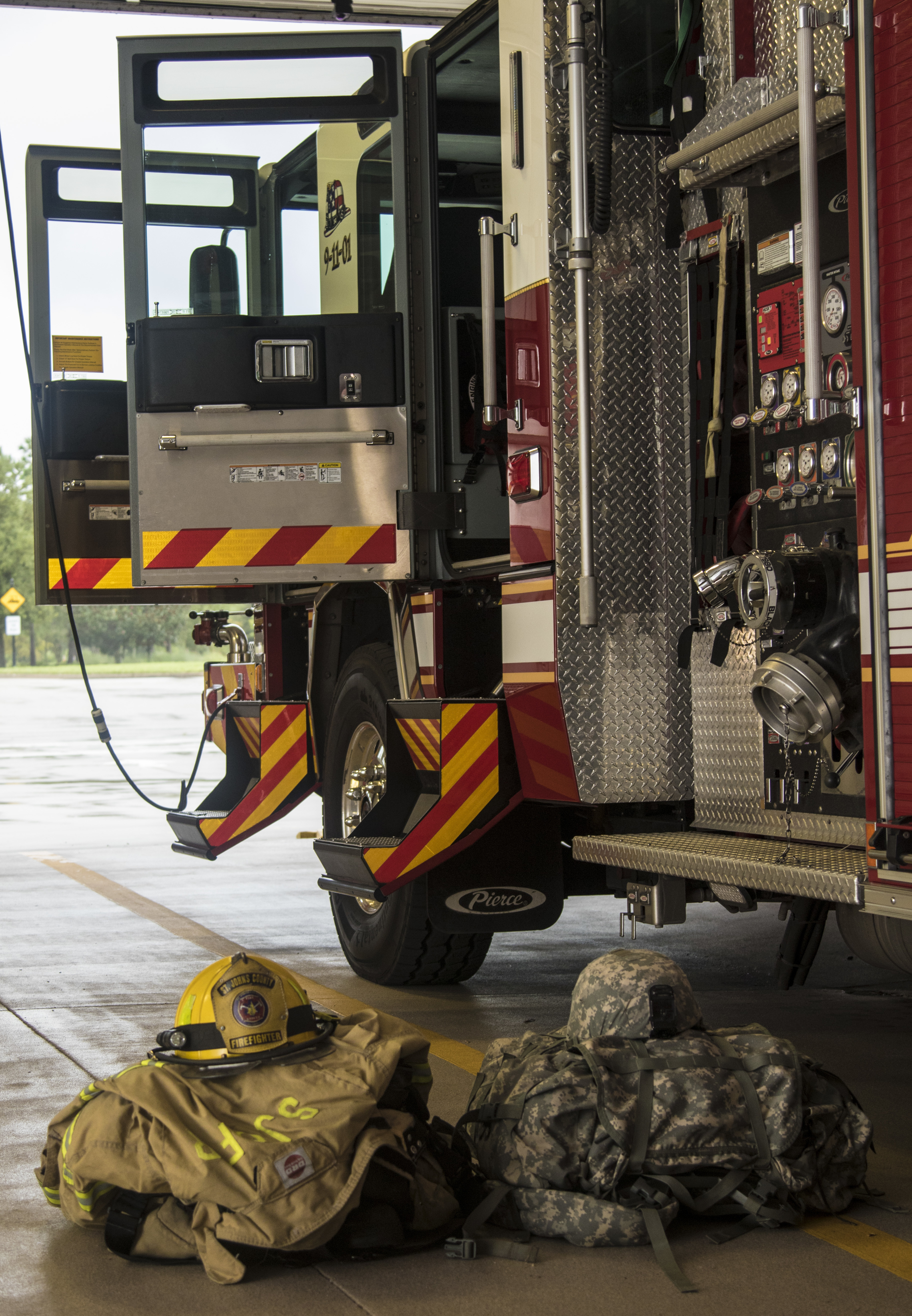 A red and white fire truck parked inside a fire station bay with gear on the floor.