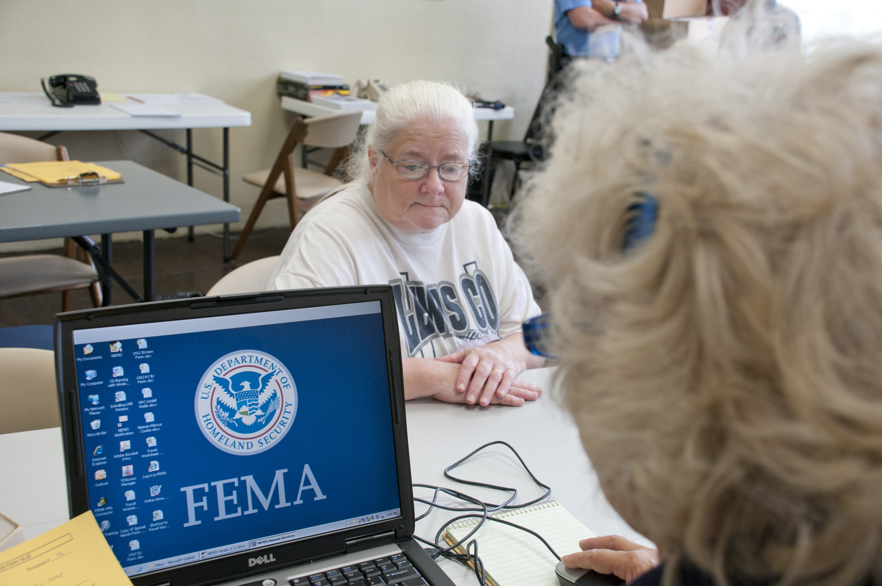 Two people seated across a table at a FEMA Disaster Recovery Center with a laptop.