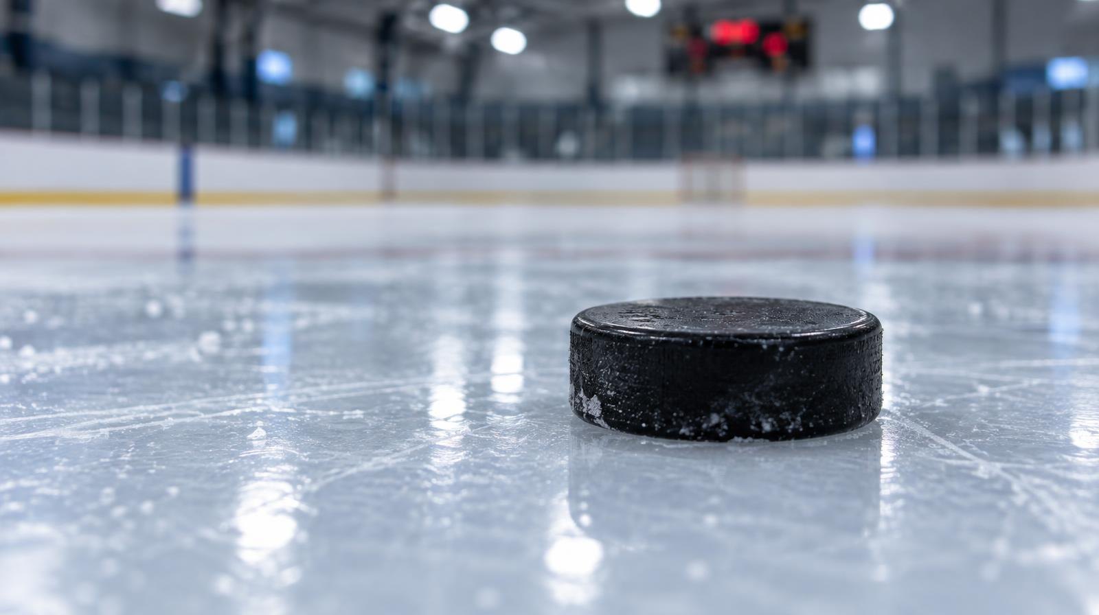 A black rubber hockey puck resting on a smooth, reflective ice surface.