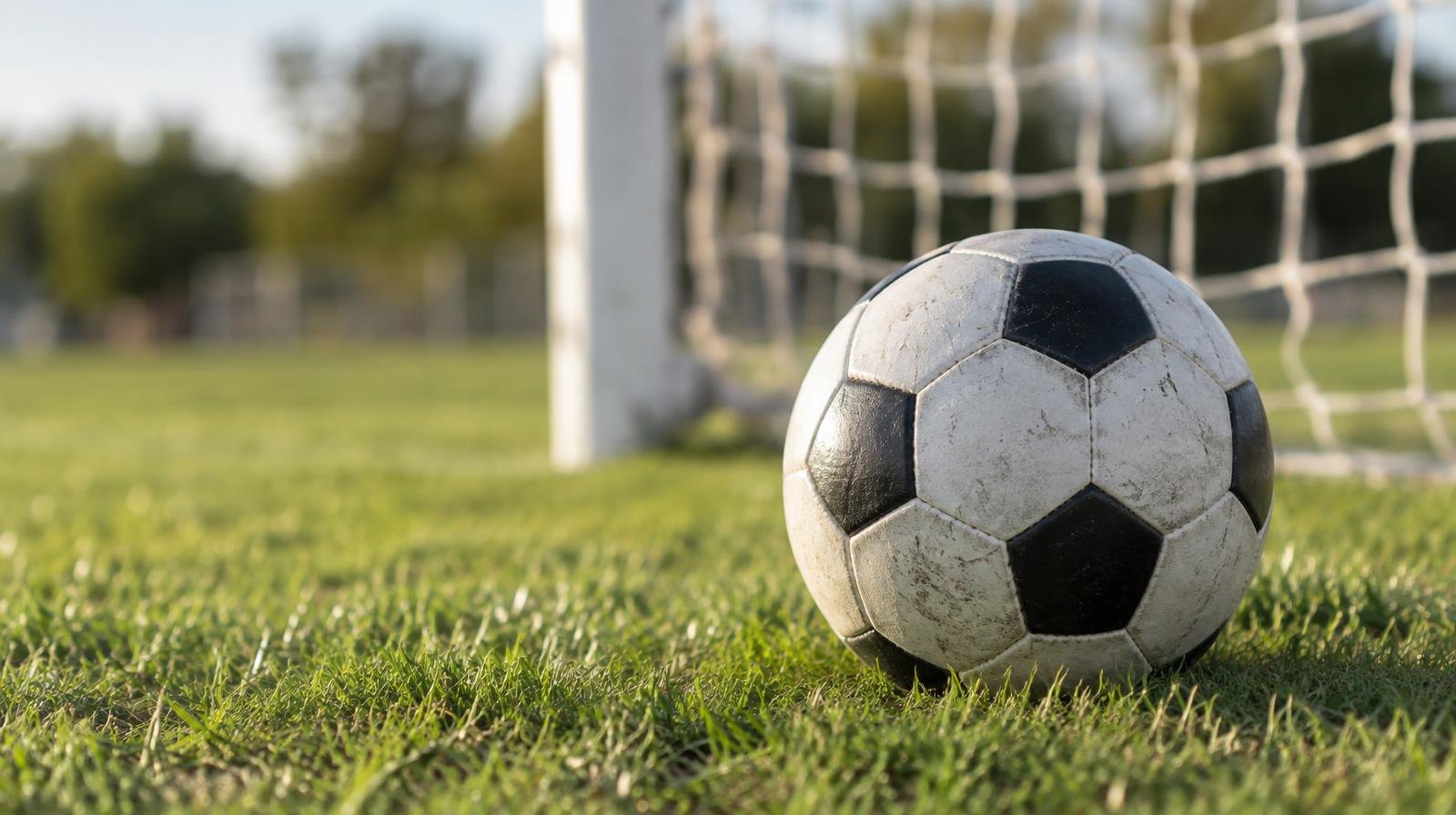 A black-and-white soccer ball resting on green grass near a goal net.
