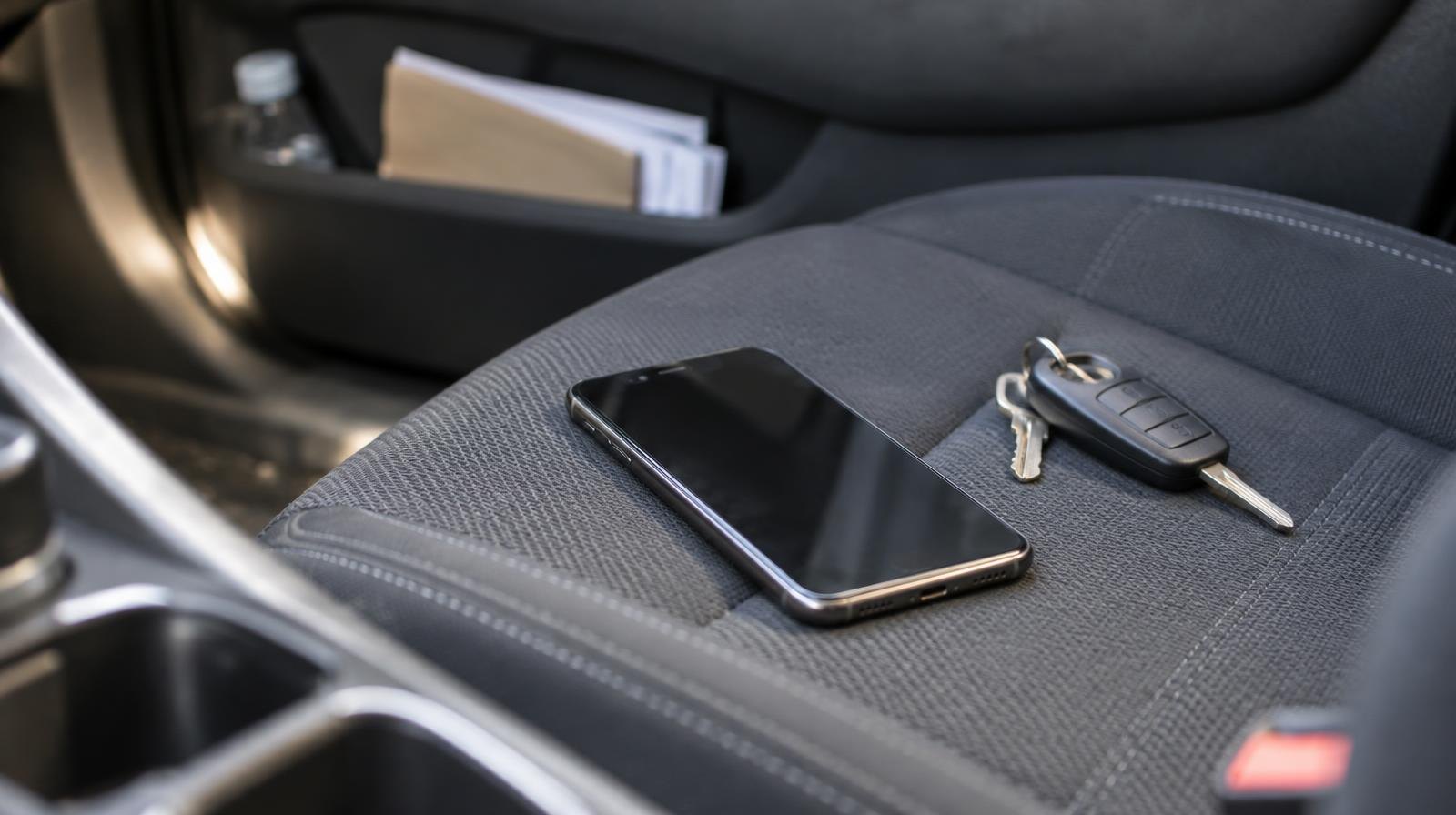 A face-down smartphone and car keys resting on a car seat in natural daylight.