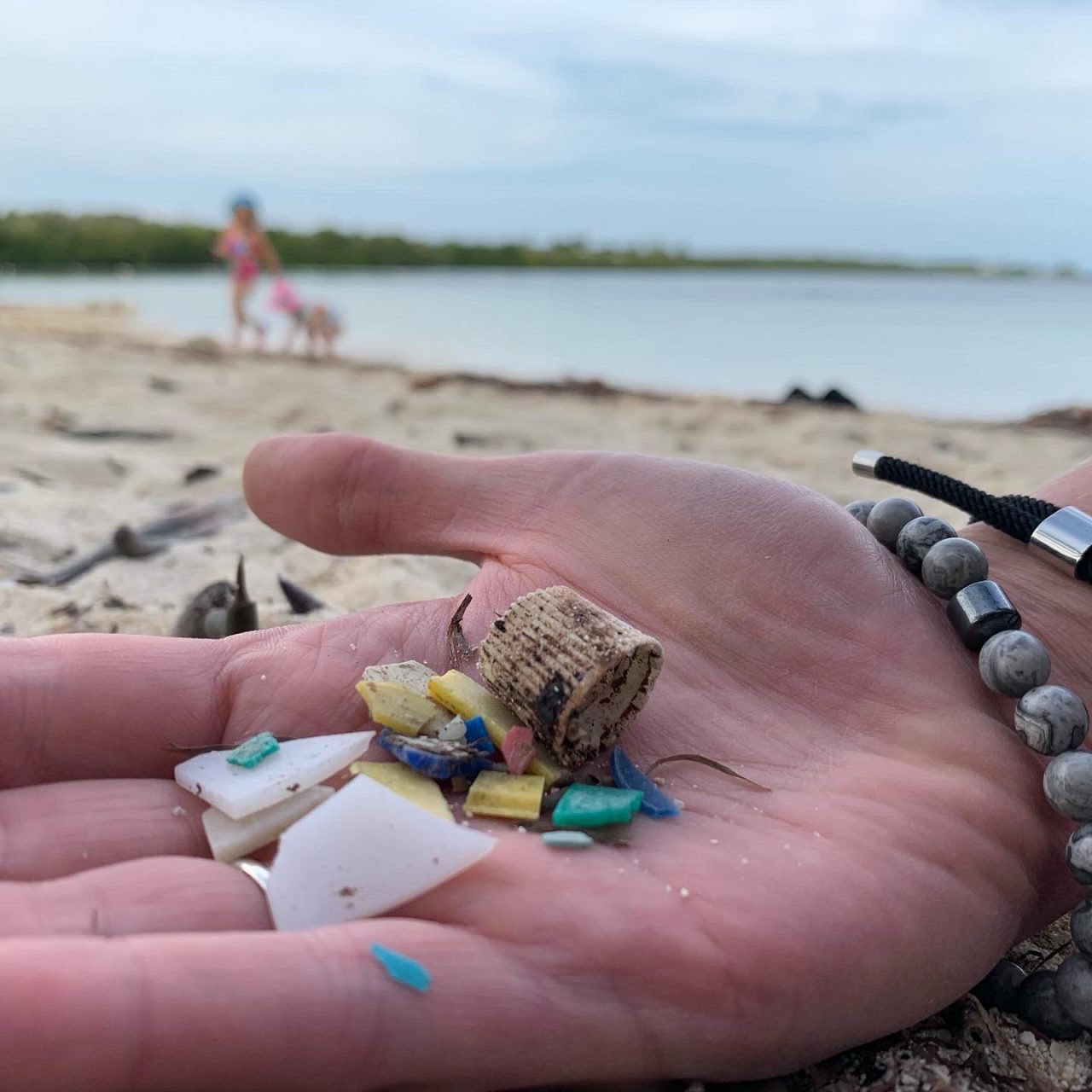 A hand holds small colorful plastic fragments gathered from a sandy beach.