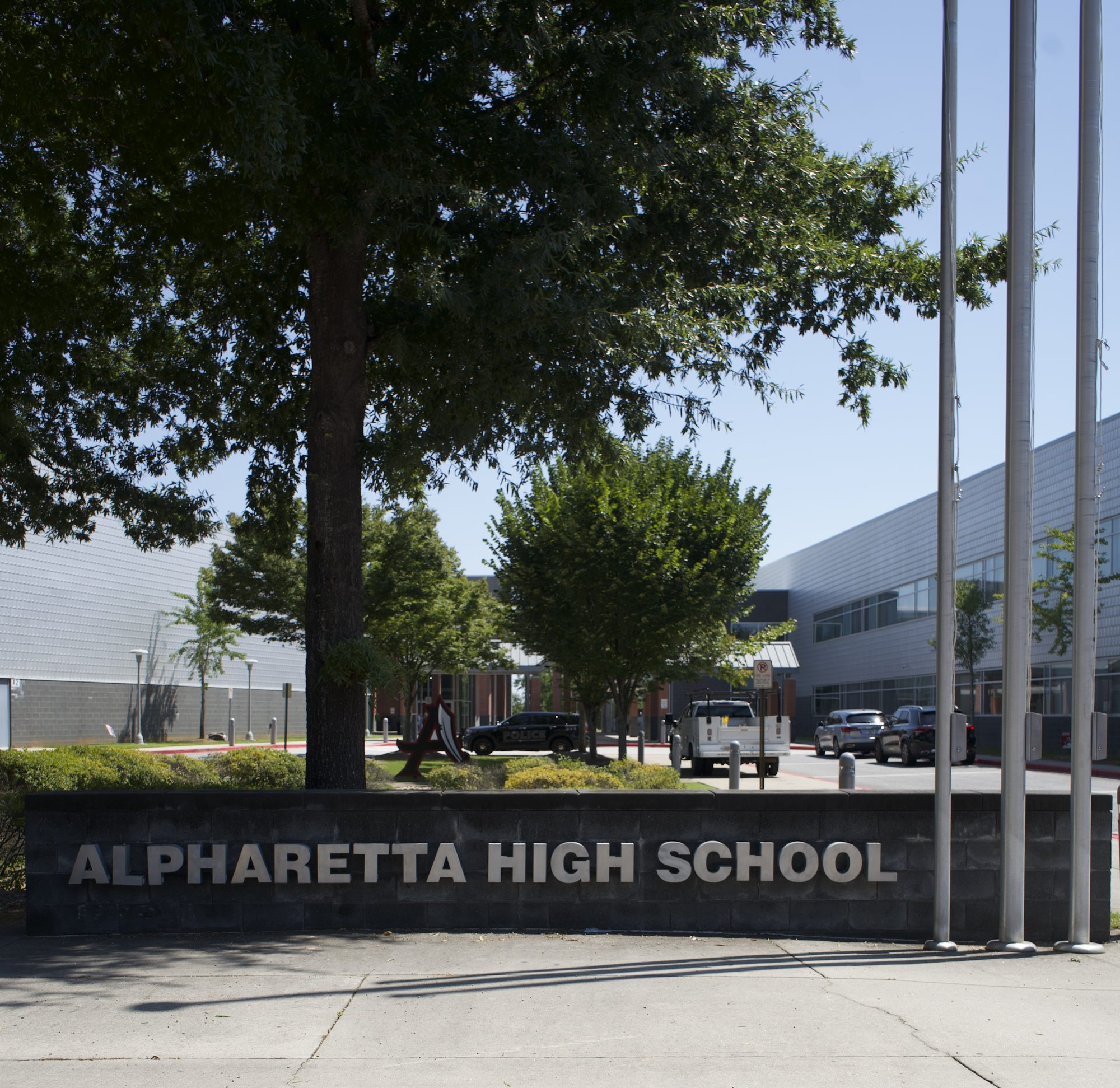 Stone monument sign at the entrance of a school campus with flagpoles and trees