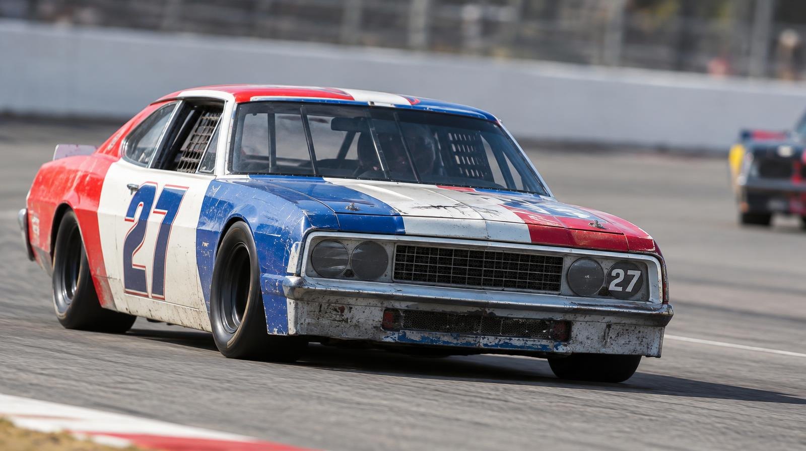 A vintage stock car speeding along an oval racing track on a sunny day.