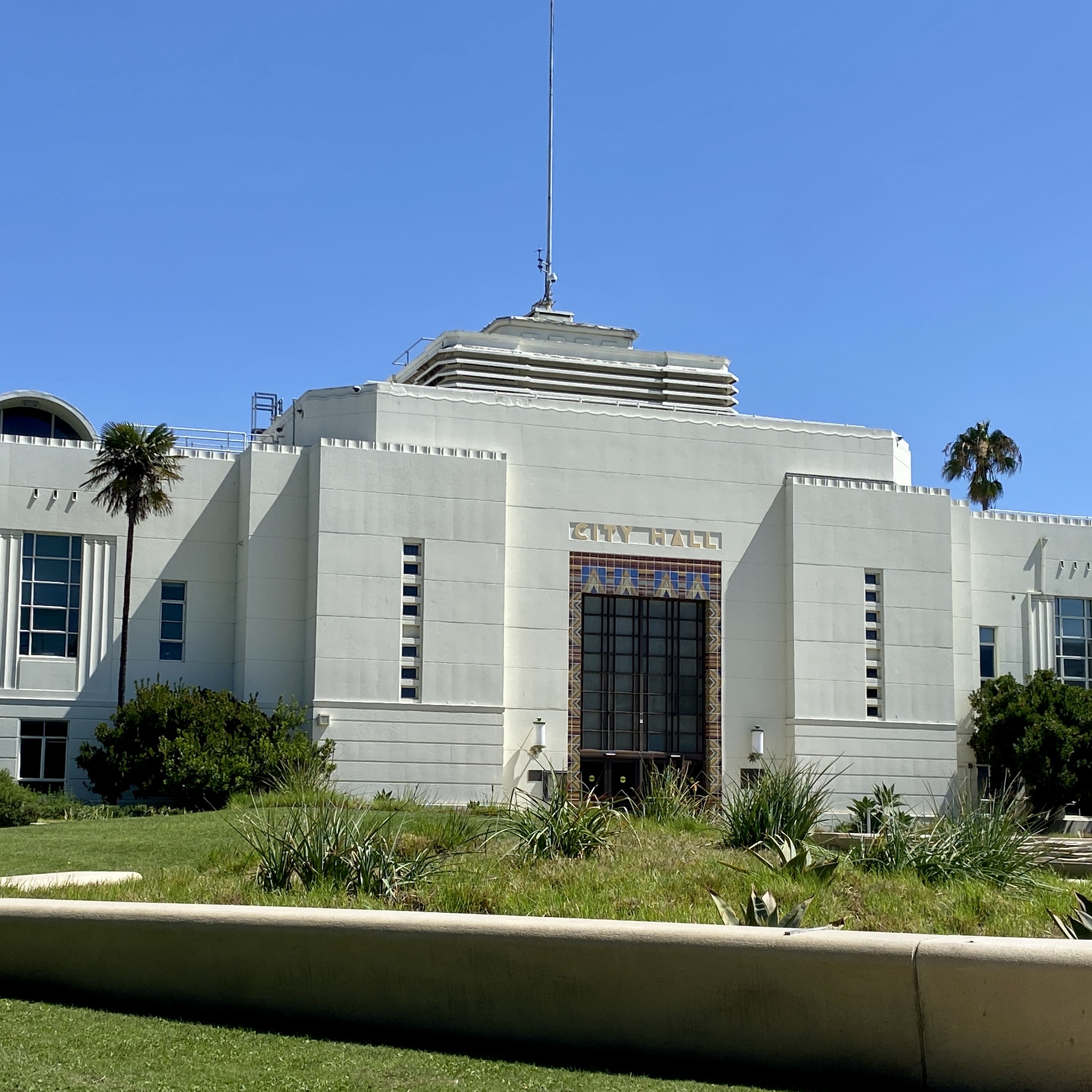 Santa Monica City Hall, a white Art Deco building with palm trees and a green lawn under a blue sky.