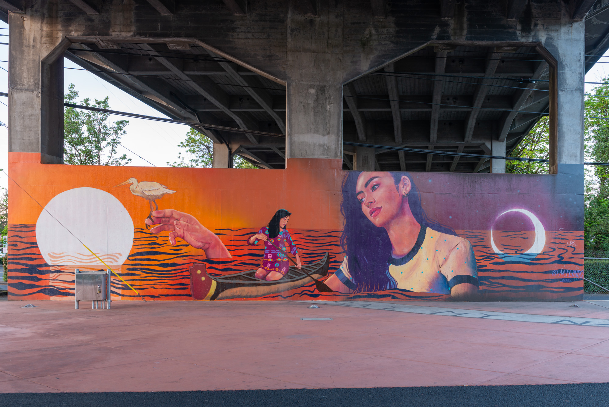Colorful mural with figures in a water scene painted on a concrete wall beneath an overpass.