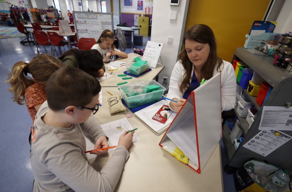 A woman reviews documents with several young children seated at a classroom table.