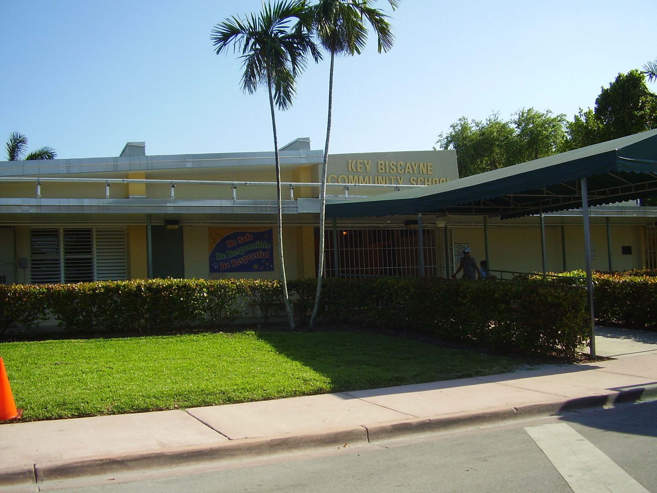 Single-story yellow school building with palm trees and a sign reading Key Biscayne Community School.