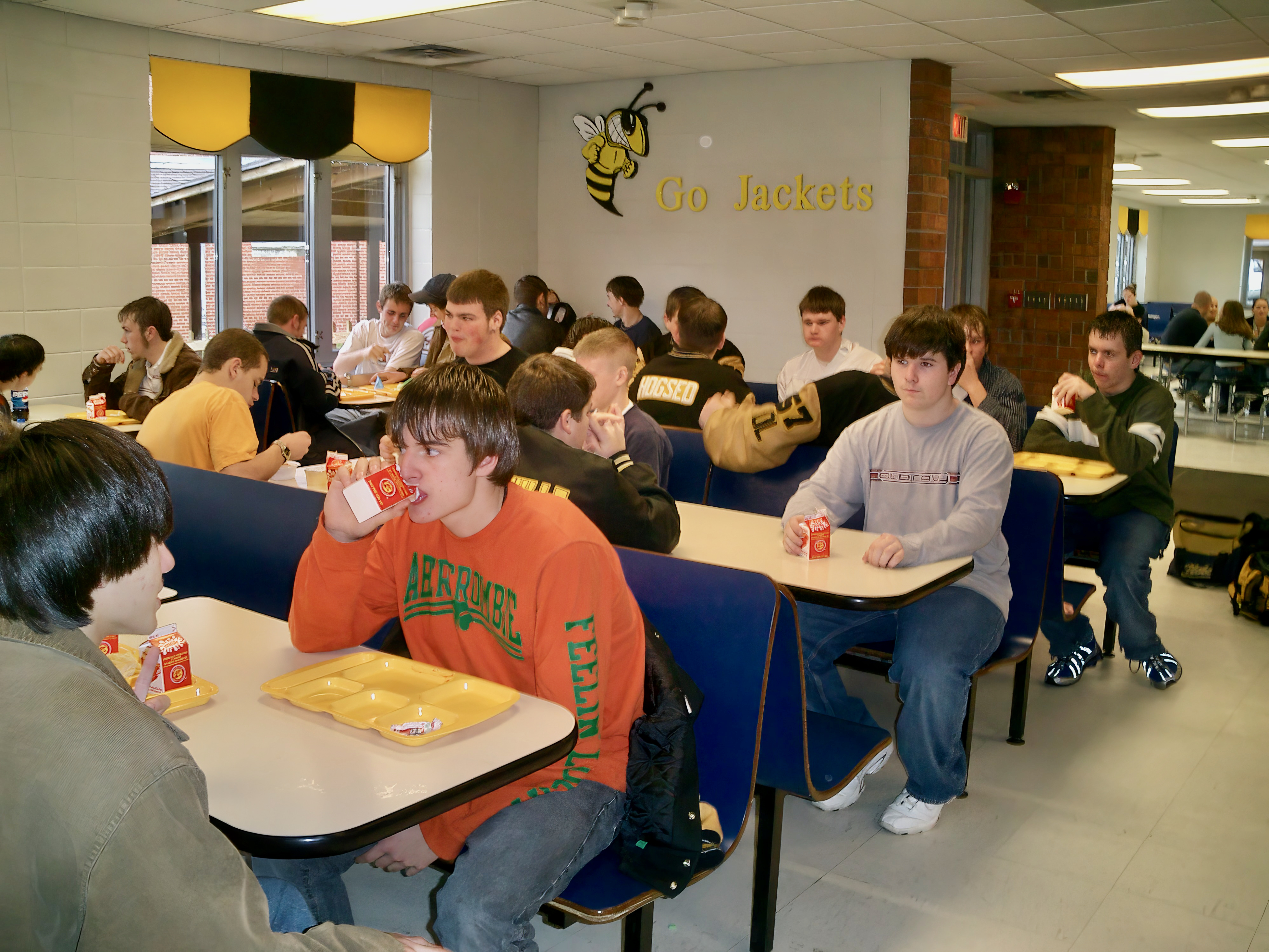 High school students eating lunch at tables in a school cafeteria.