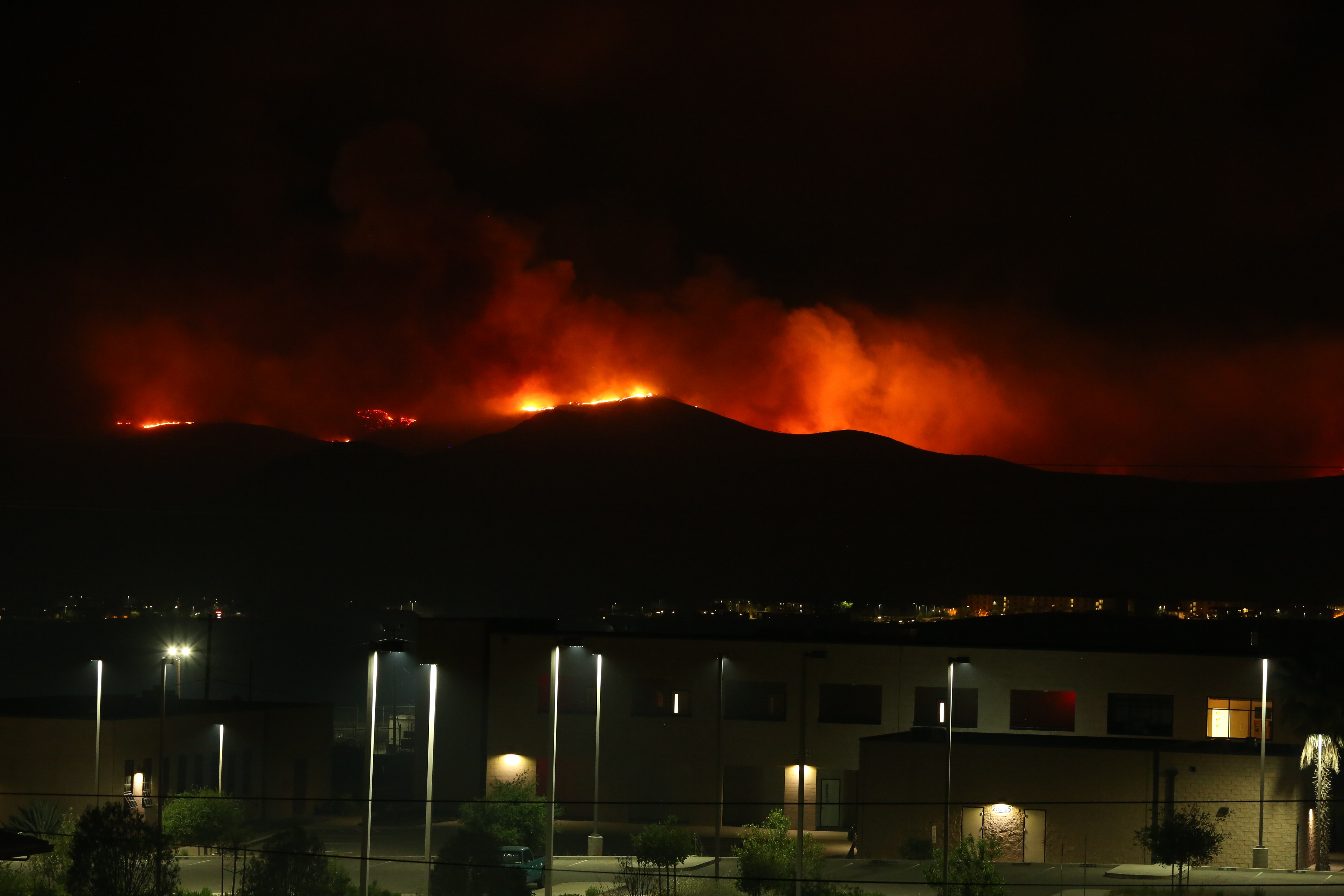 Orange flames and smoke light up the night sky along a hillside ridge.