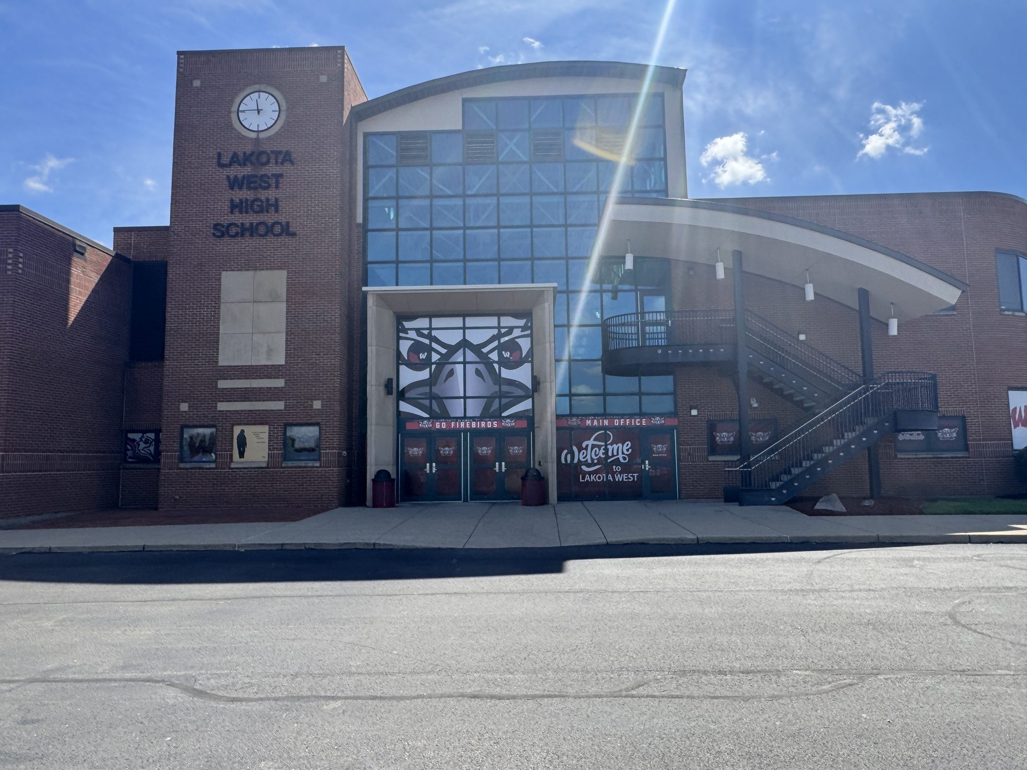 Brick high school building with a glass-and-steel entrance atrium on a sunny day.