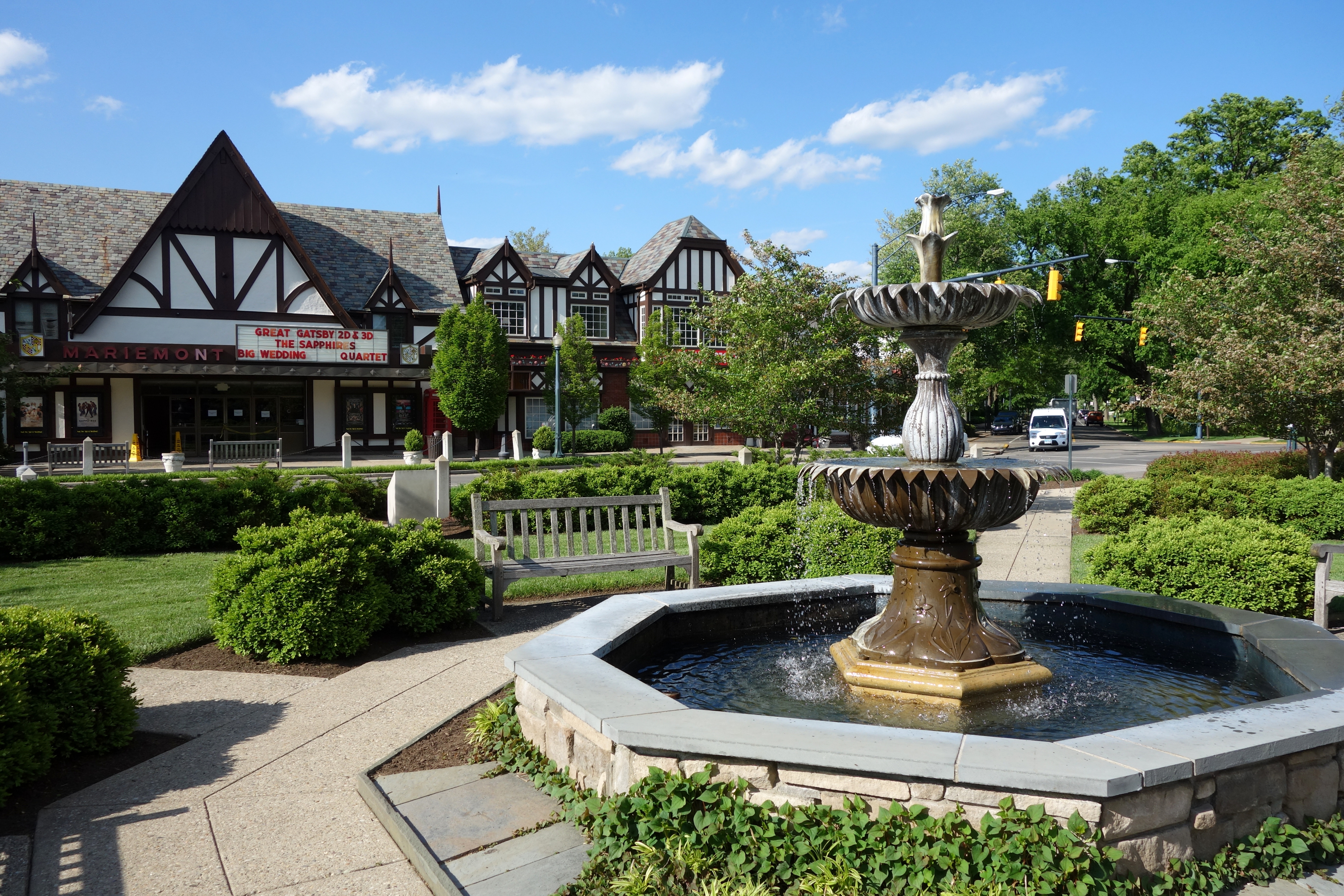 Stone fountain in a landscaped plaza with Tudor-style brick buildings behind it.