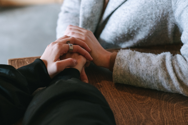 Two people holding hands across a wooden table indoors.