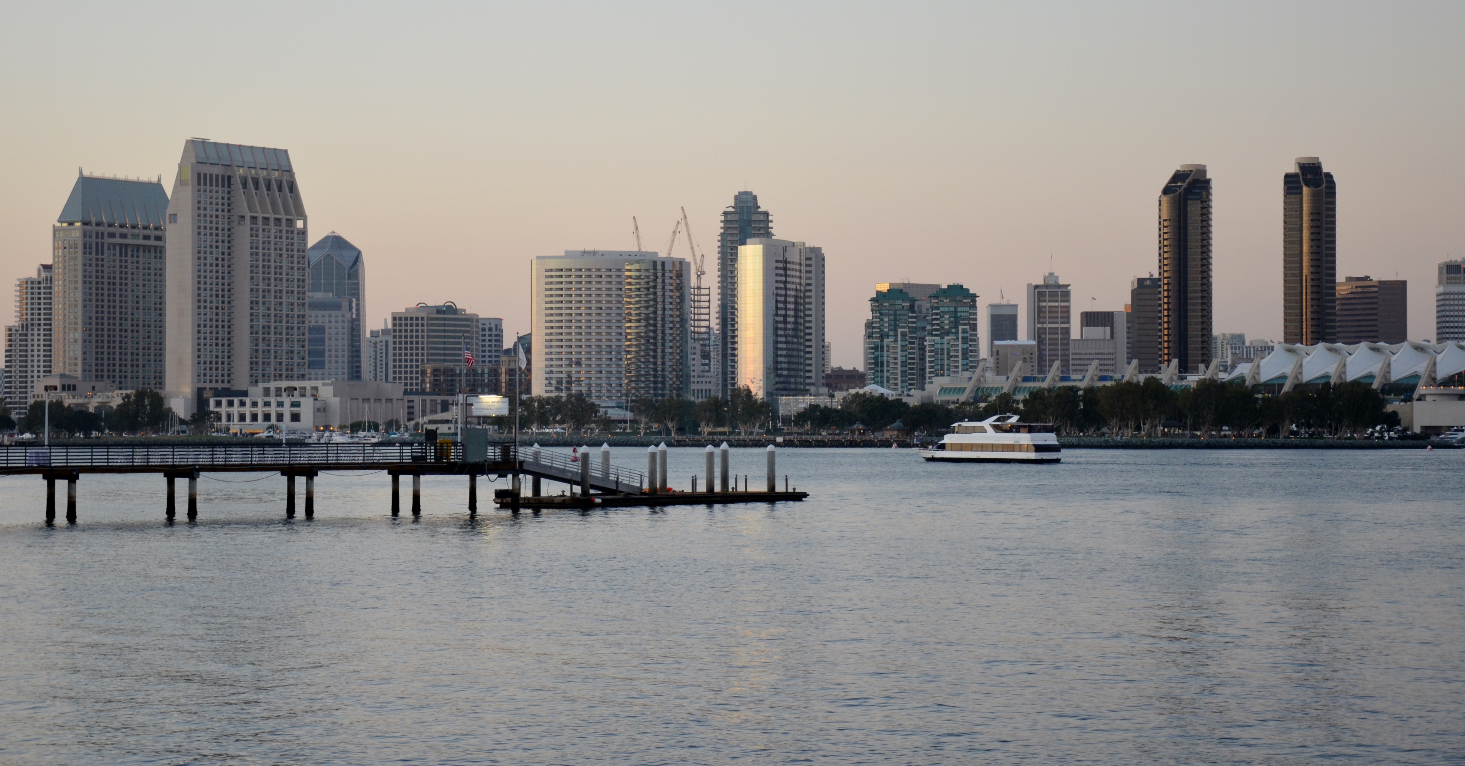 White passenger ferry on a calm bay at dusk with a city skyline in the background.