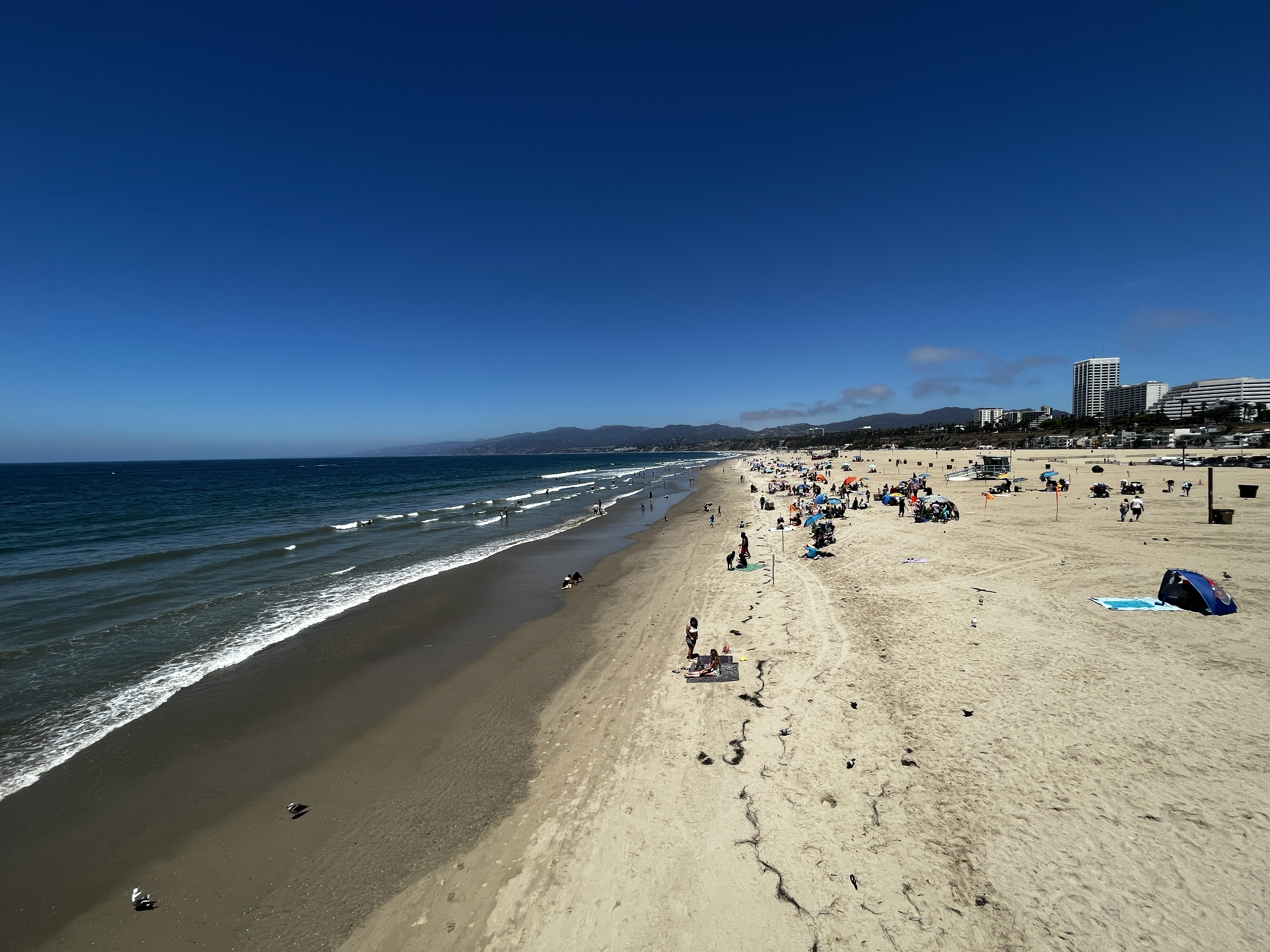 Wide sandy beach with gentle surf and scattered beachgoers under a clear blue sky.