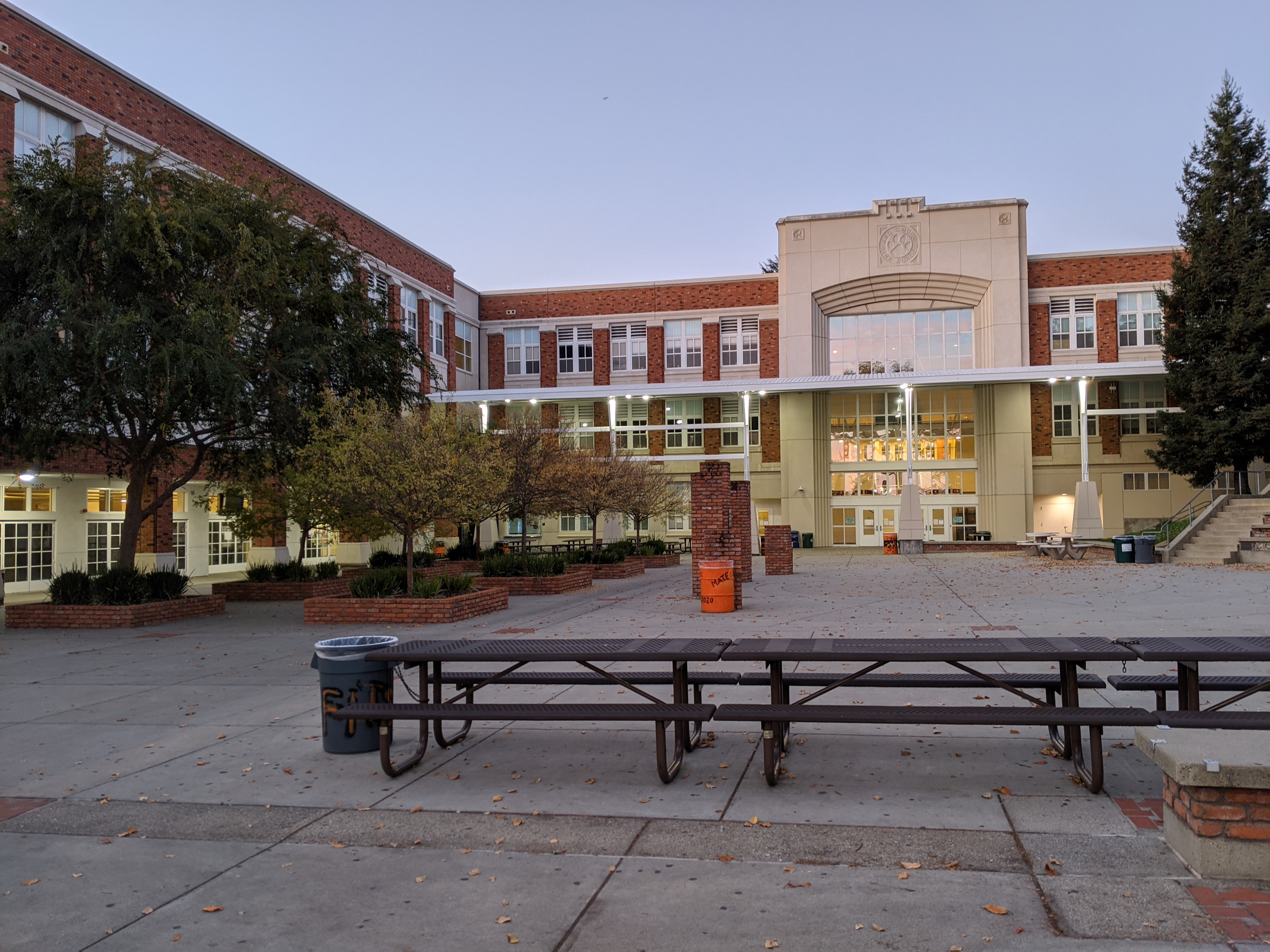 Brick high school building courtyard with picnic tables and trees at dusk.