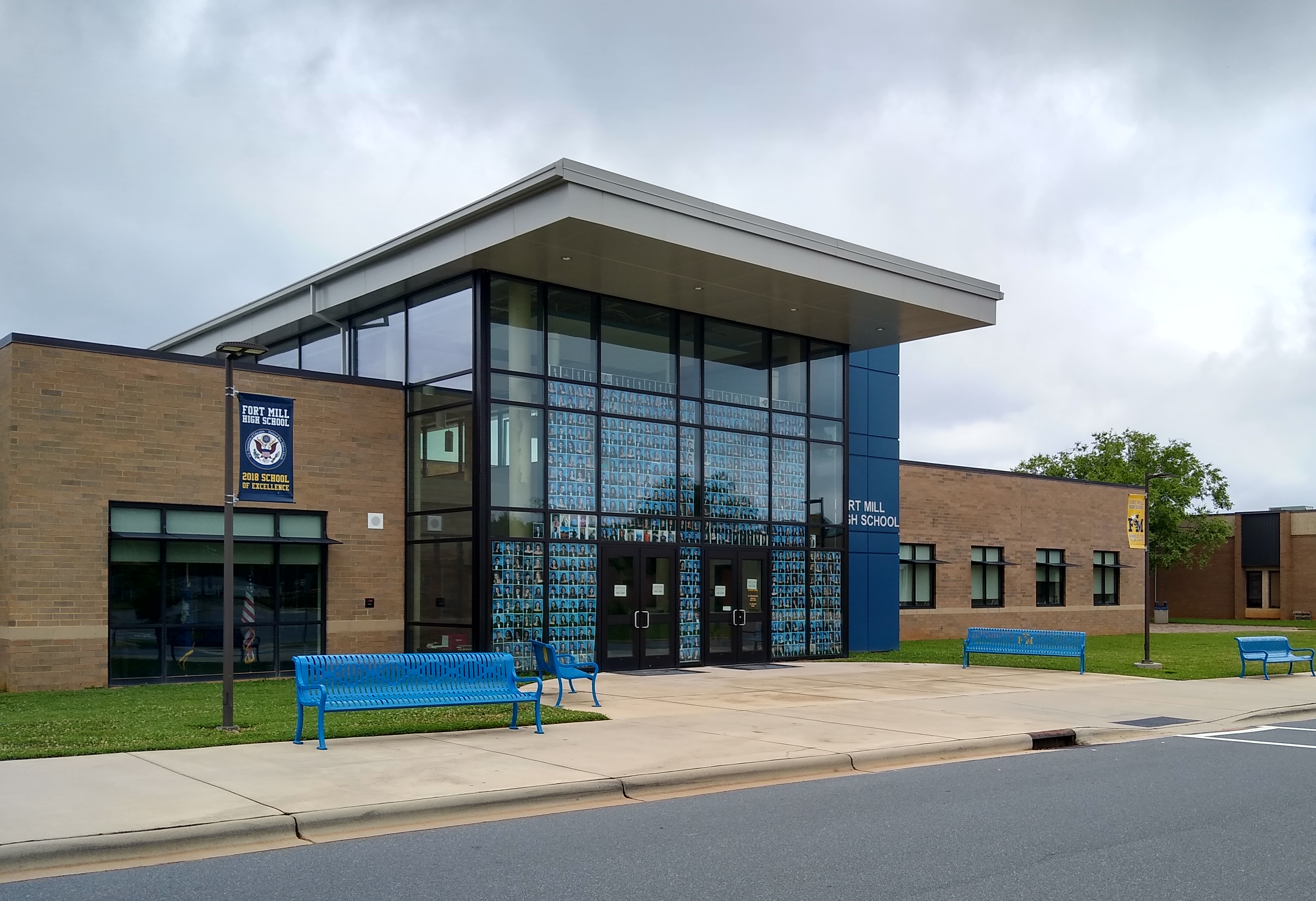 Exterior of a school building with a glass entrance facade and blue benches.