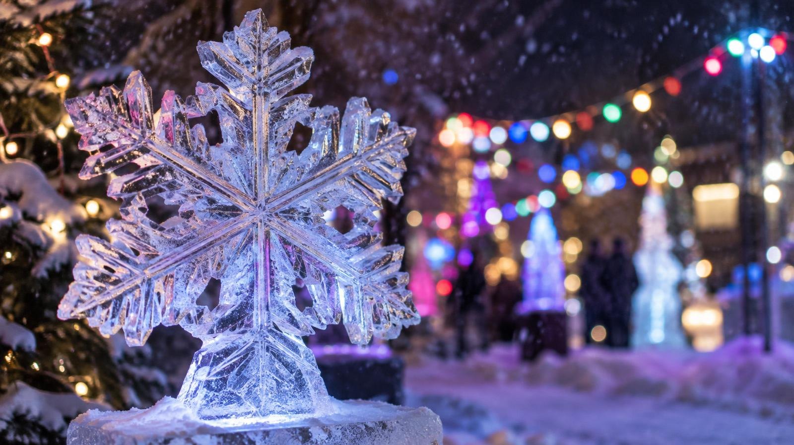 A glowing ice sculpture surrounded by colorful lights and fresh snow at night.