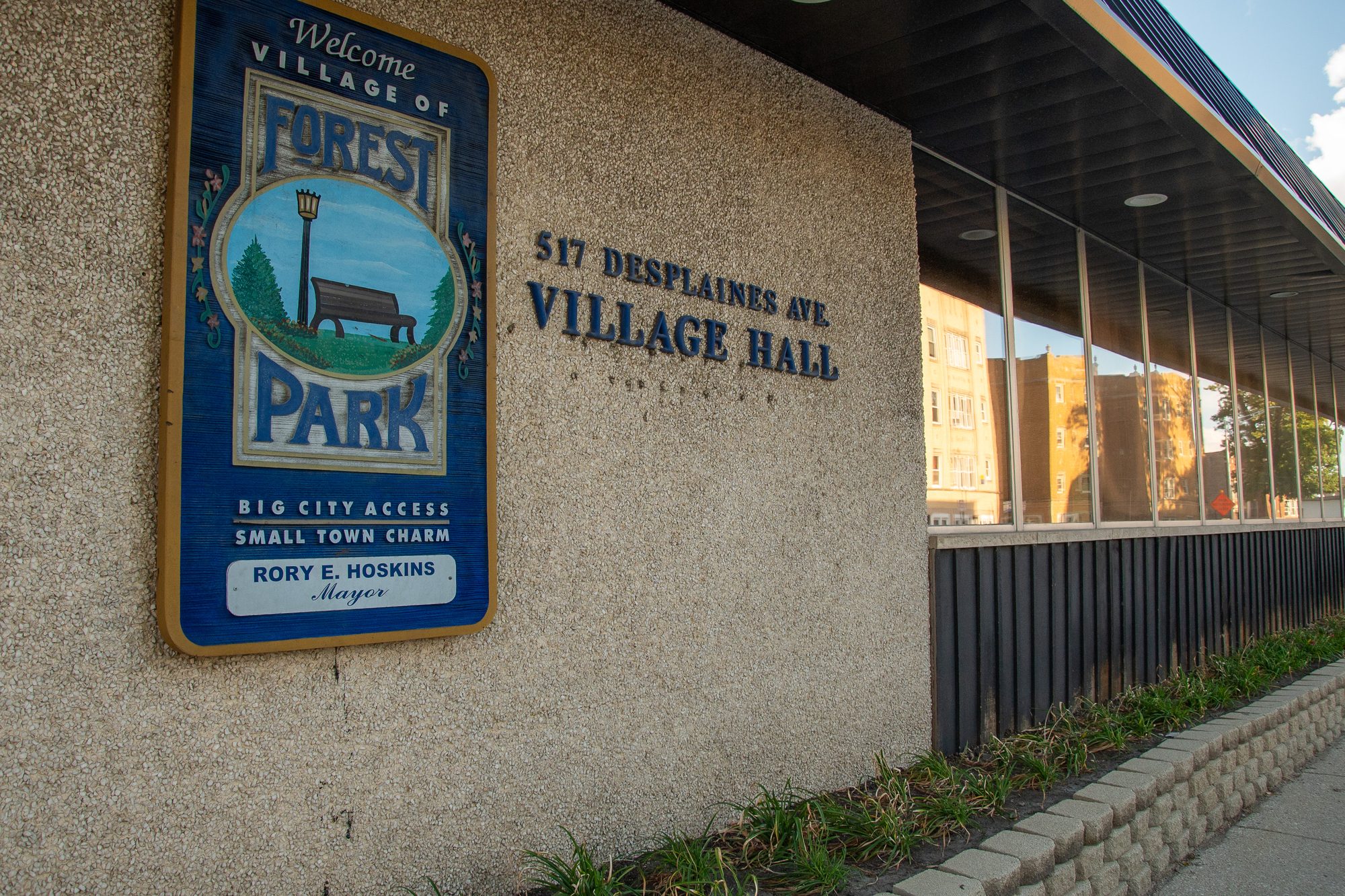 Exterior wall of a village hall building with a painted welcome sign and address numbers.