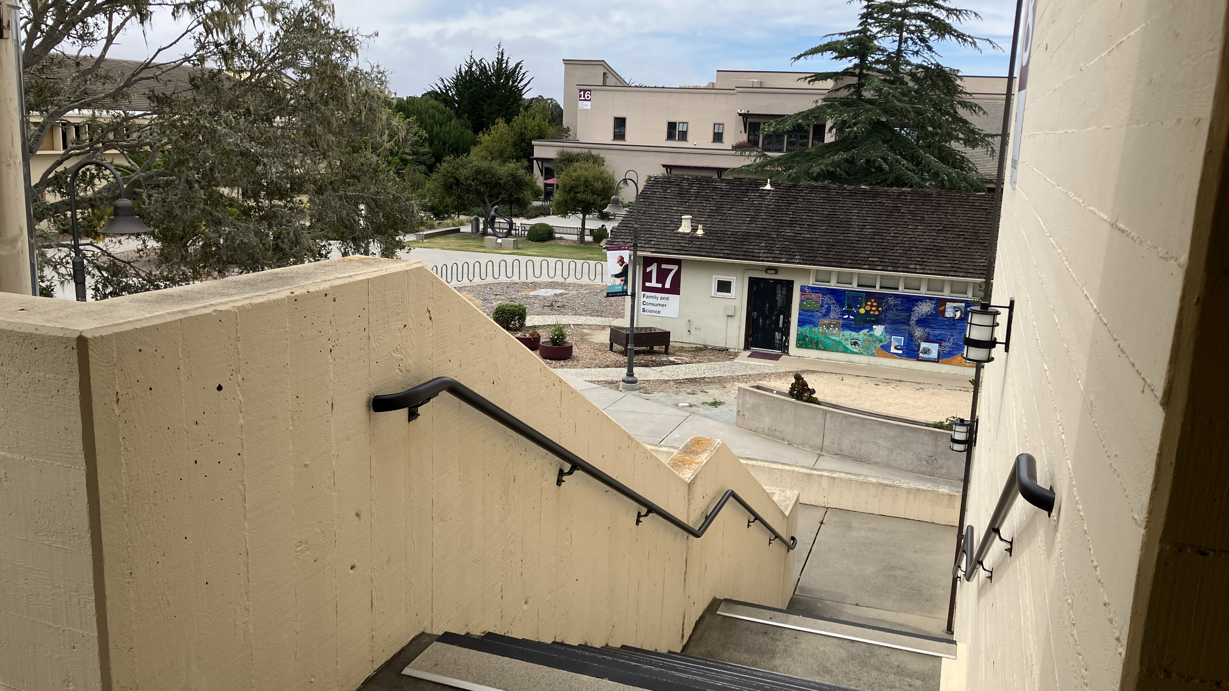 Outdoor staircase descending from a campus building with other college buildings and trees in the background.