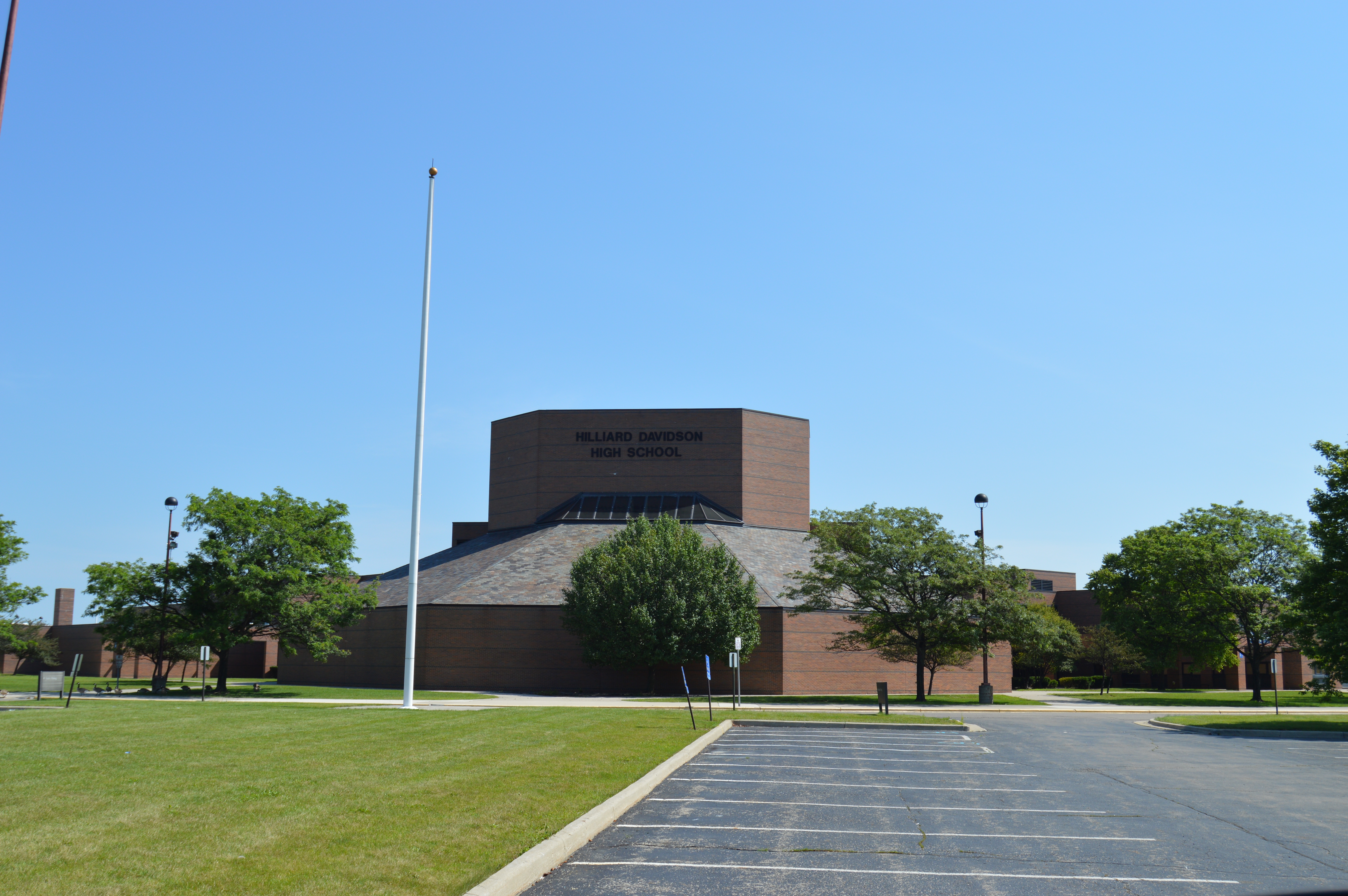 Brick school building exterior with flagpole and parking lot under a clear blue sky.