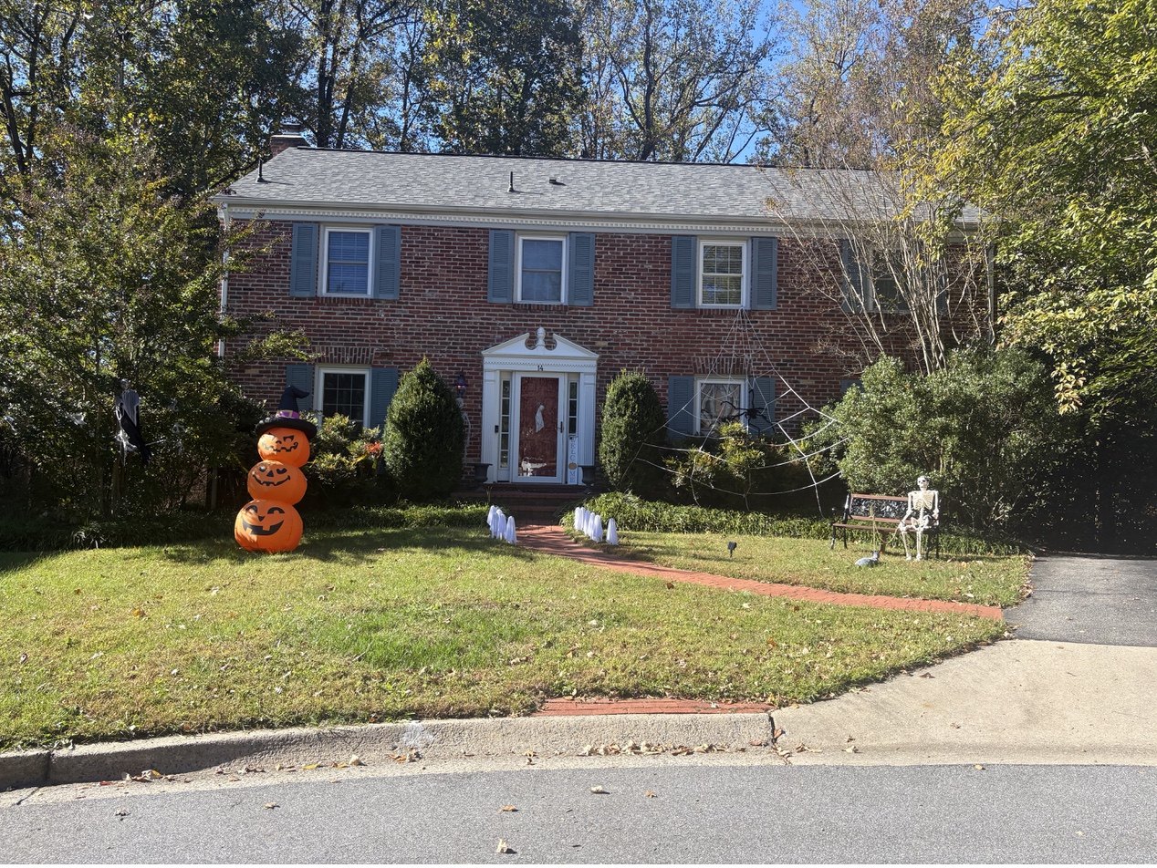 Brick colonial house decorated for Halloween with inflatable pumpkins, ghost figures, and cobwebs.
