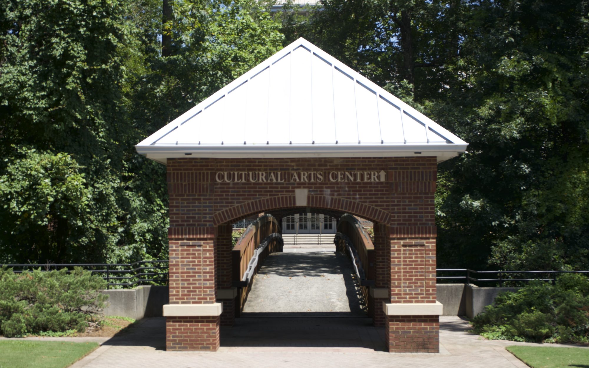 Brick arched gateway with white roof leading to a covered pedestrian bridge