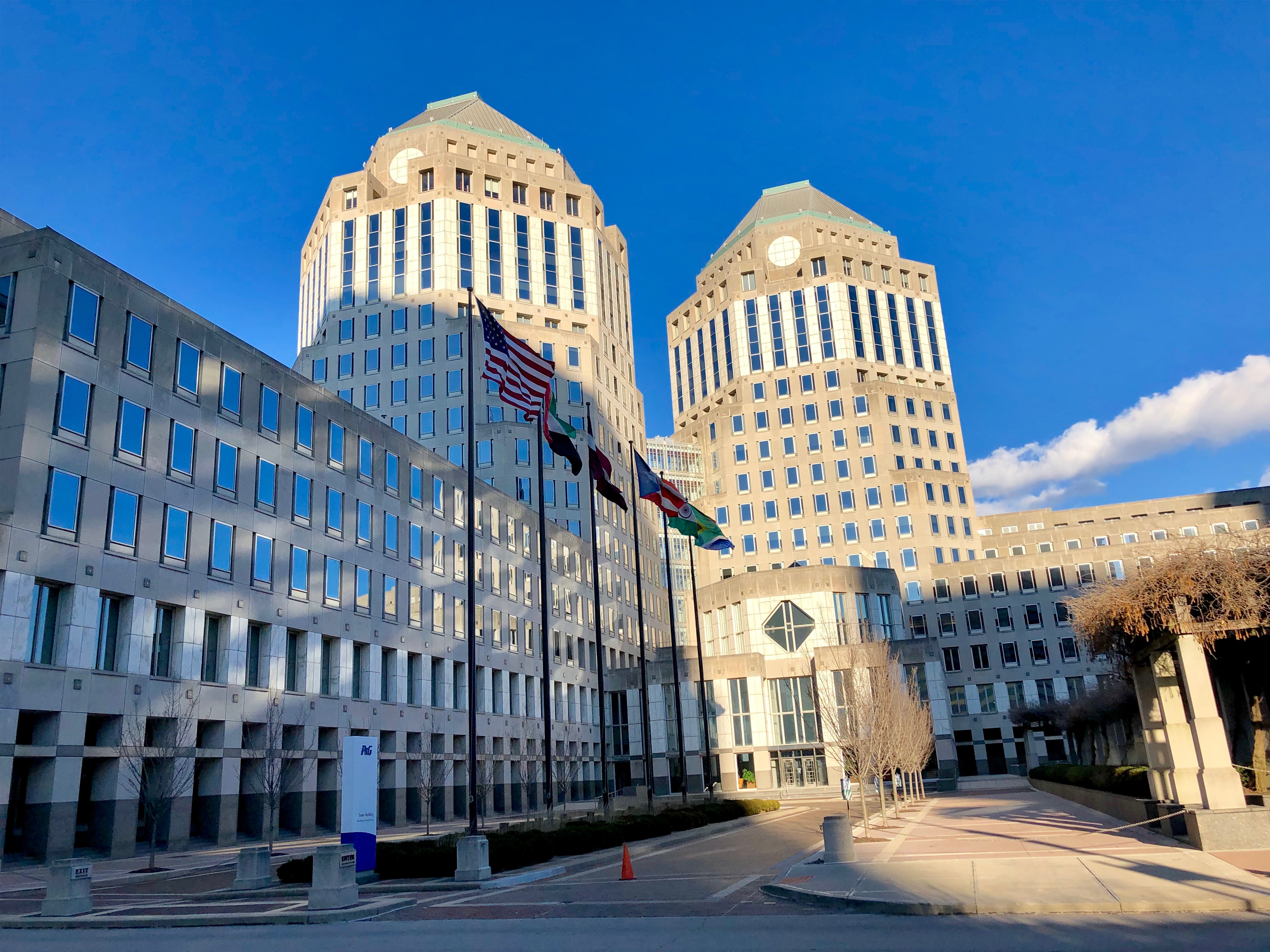 Two tall corporate office towers with flags on flagpoles under a clear blue sky.