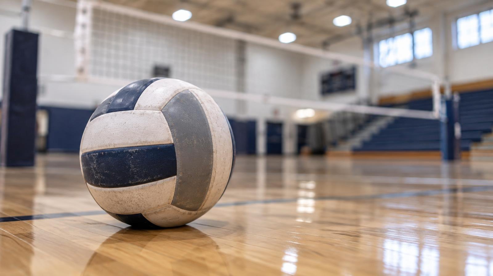 A volleyball sitting on a hardwood gym floor near the net.