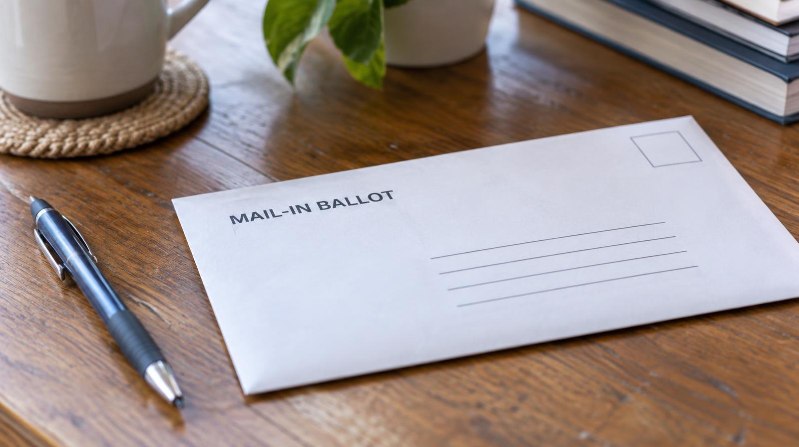 A blank envelope and pen resting on a wooden table in soft natural light.