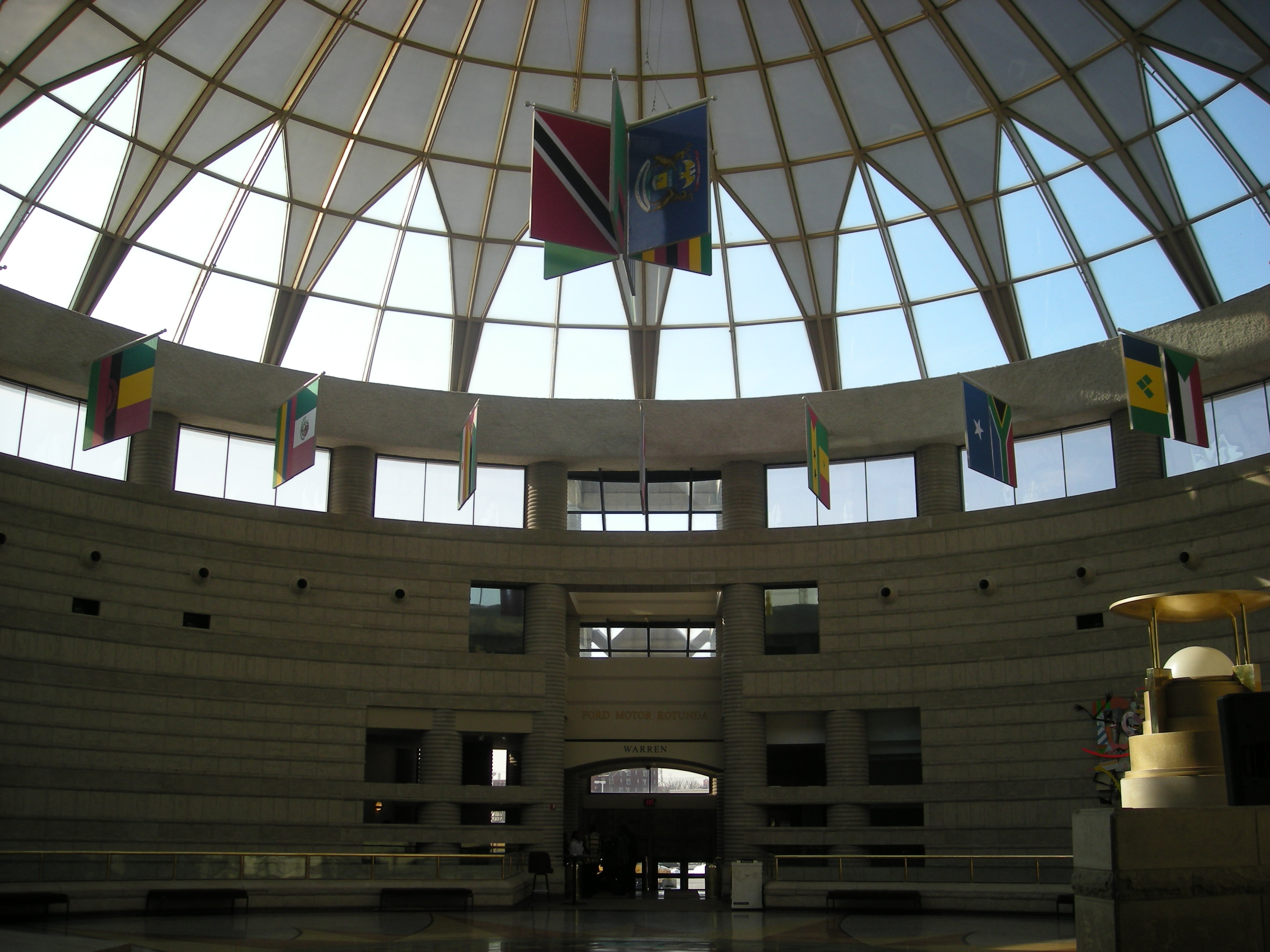Interior rotunda of a museum with a large domed skylight and colorful flags hanging from the ceiling.