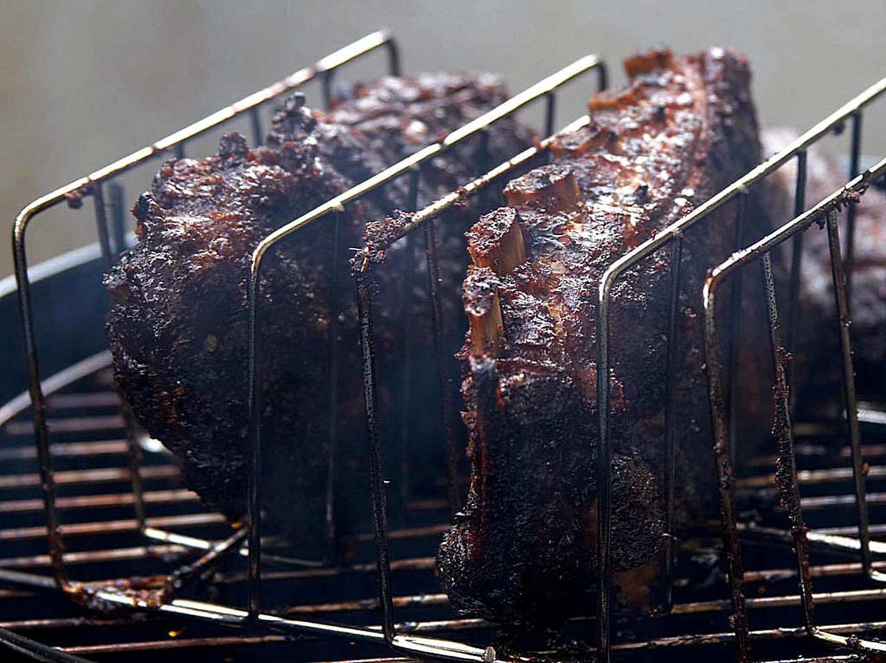 Several racks of smoked ribs standing upright in a metal rib rack on a grill, with smoke rising.