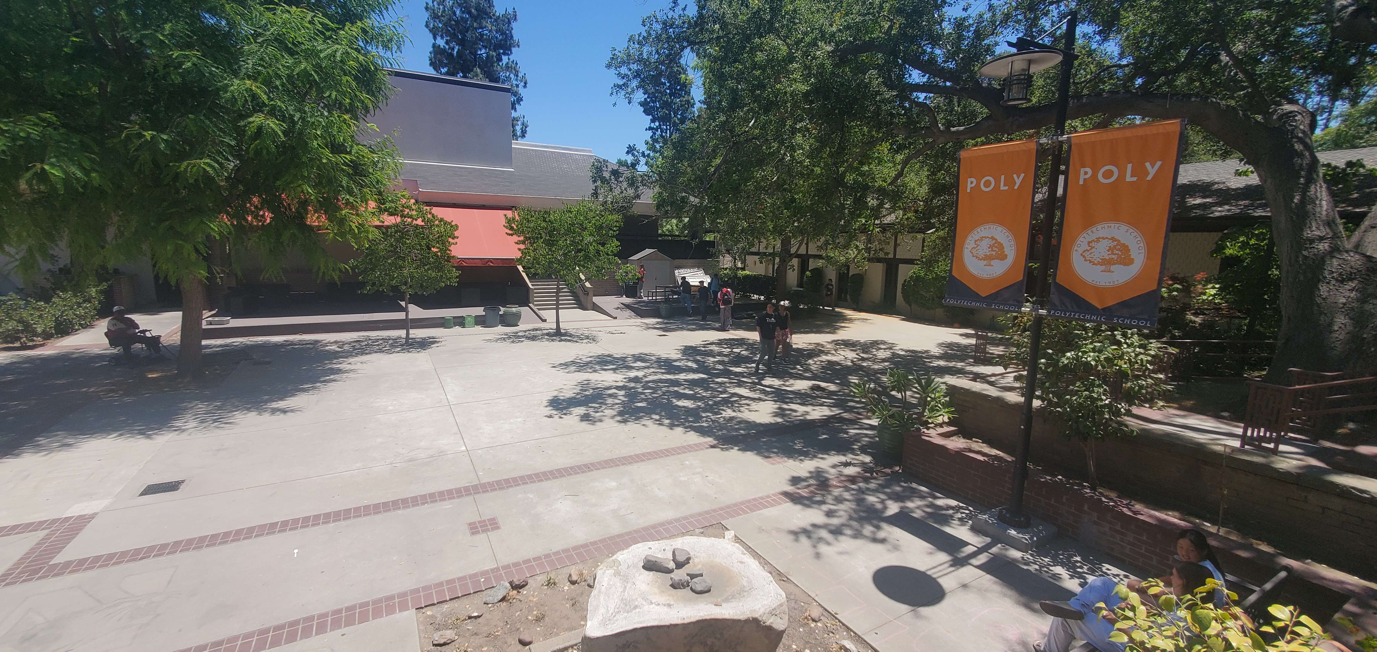 Shaded outdoor courtyard with orange banners reading POLY and brick paving.