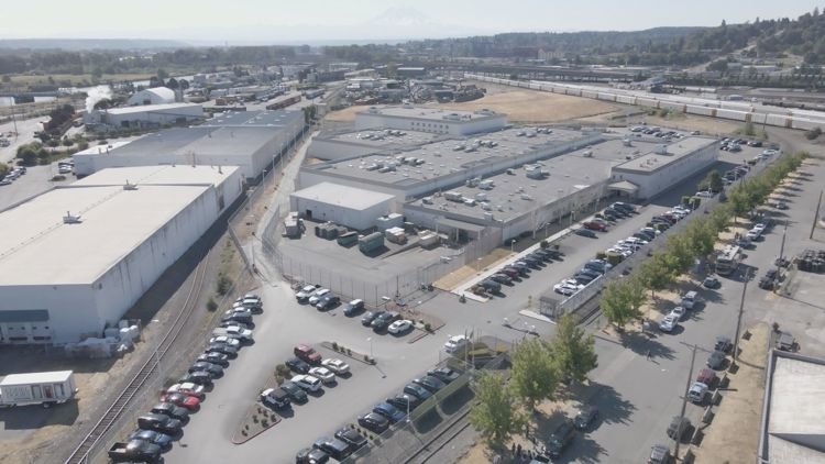 Aerial view of a large detention facility complex with multiple buildings, parking lots, and railroad tracks nearby.