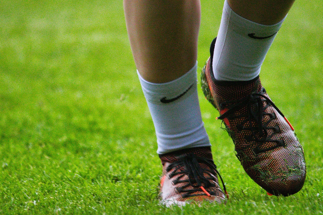 Close-up of a soccer player's feet and cleats on a grass field, wearing orange and black cleats with white socks.
