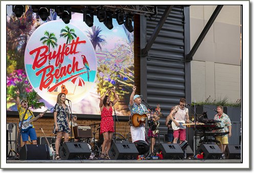 Band performs on outdoor stage with a large LED screen displaying a tropical logo.