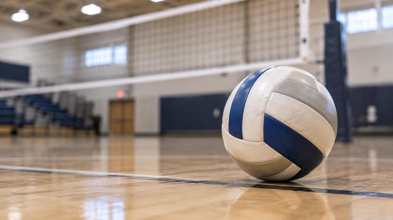 A volleyball resting on a hardwood gym floor near the net.
