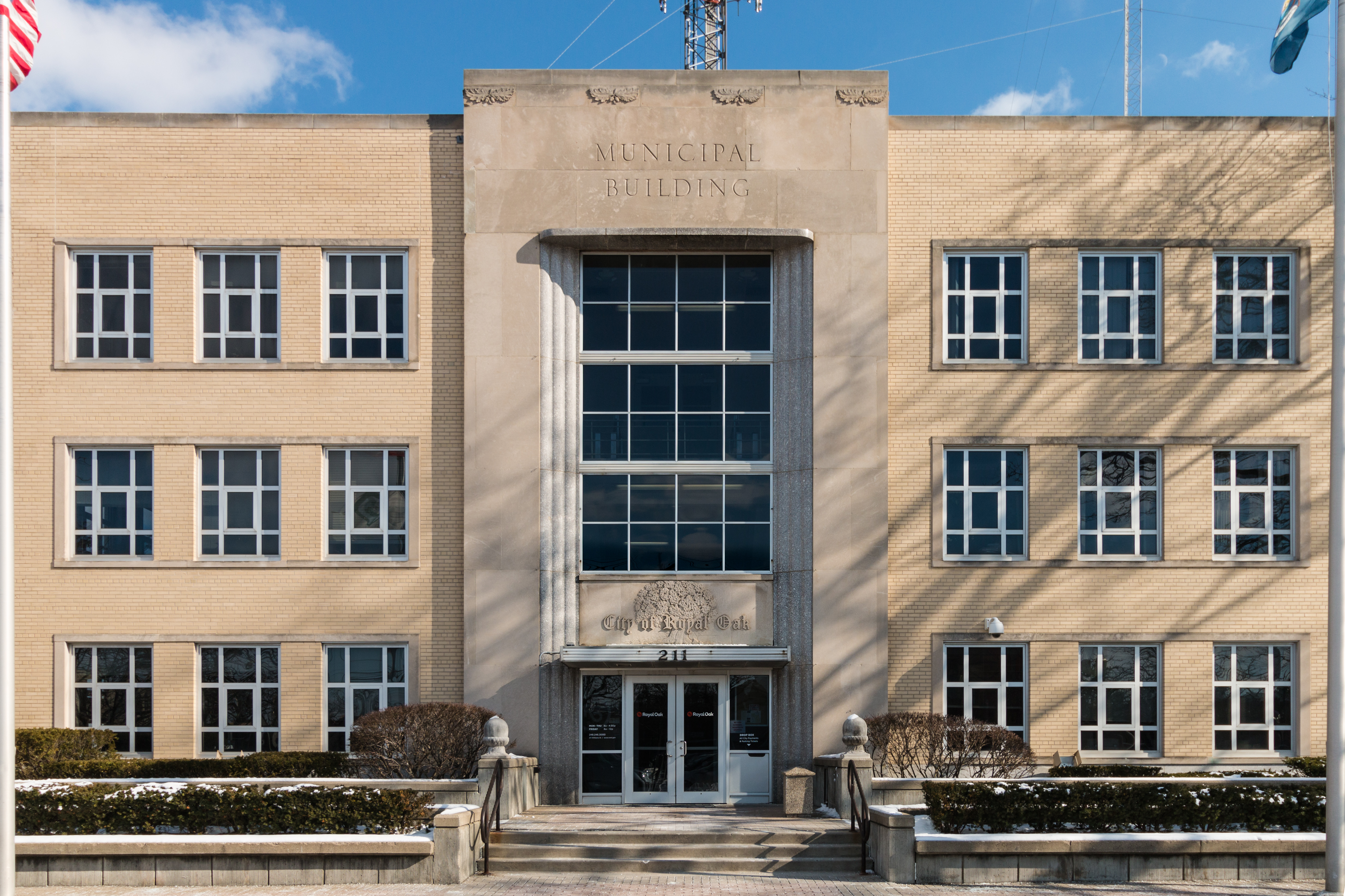 Art Deco beige municipal building with engraved entrance and American flag, light snow on ground.