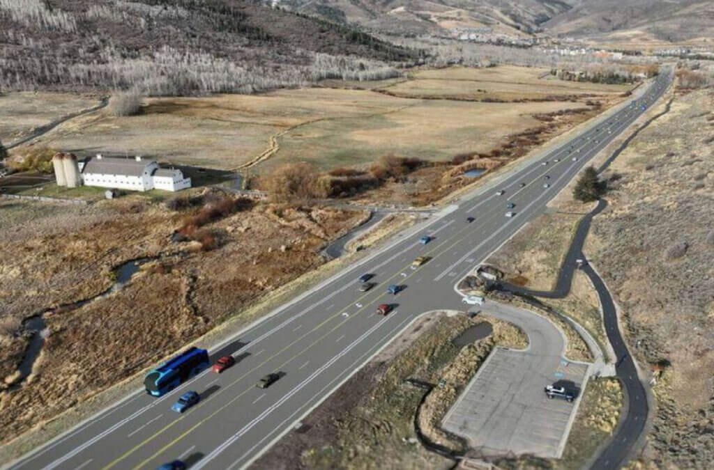 Aerial rendering of a multi-lane highway through a mountain valley with a white barn and a transit stop.