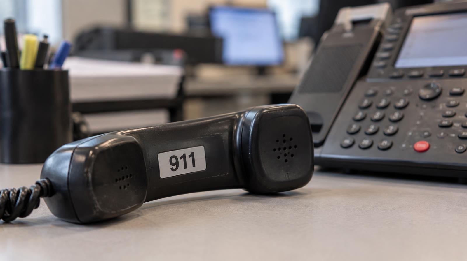 A 911 emergency telephone handset resting beside a desk phone.