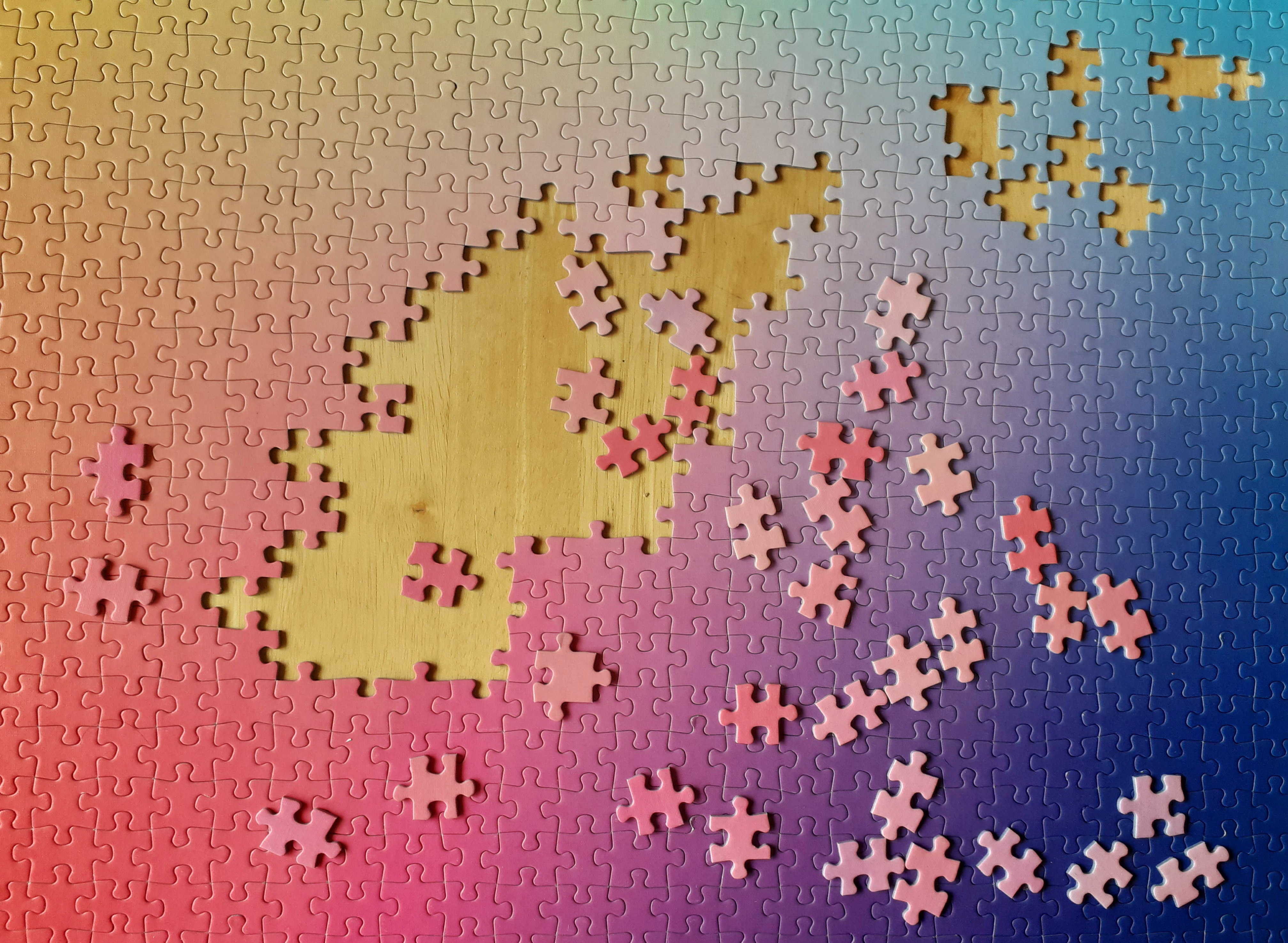 A colorful gradient jigsaw puzzle partially assembled on a wooden table with loose pieces scattered around.