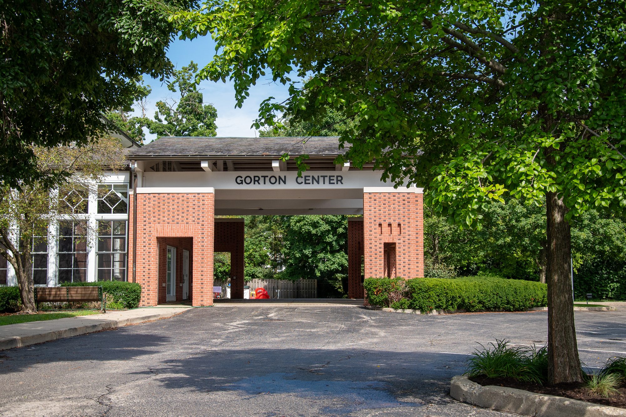 Brick entrance gateway with a sign reading Gorton Center, surrounded by mature trees.