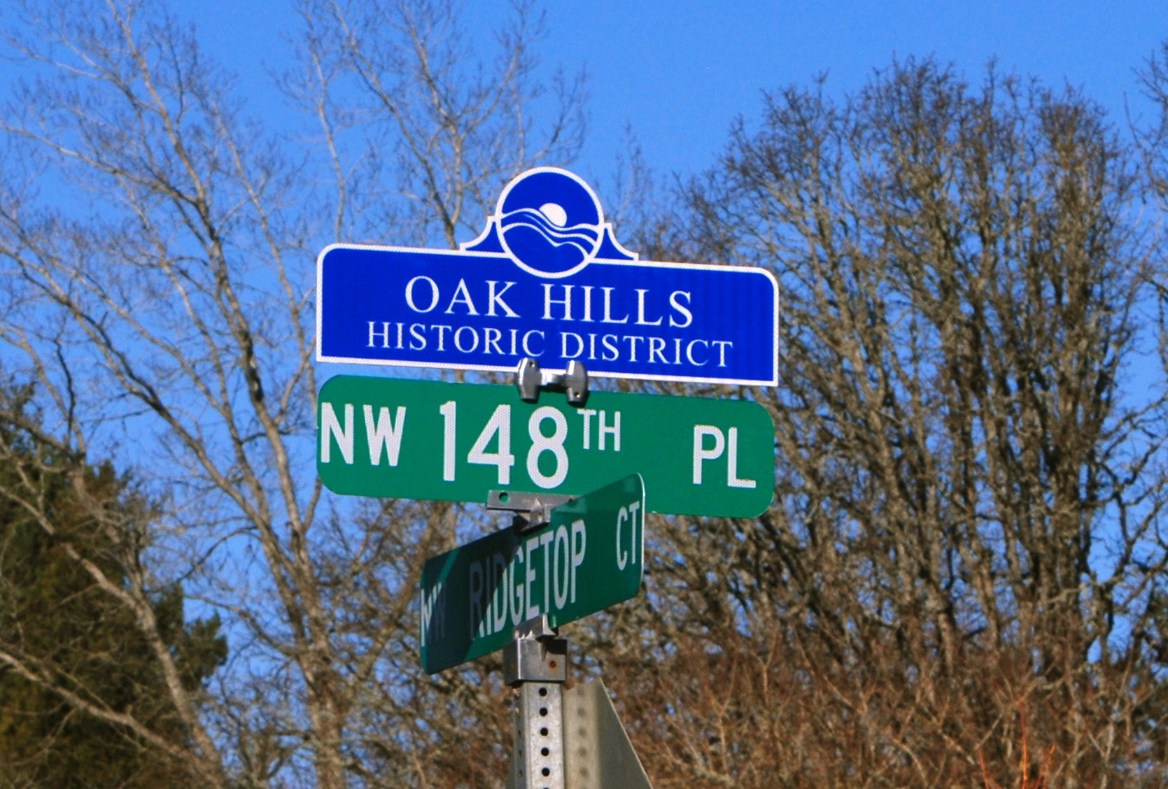 Blue neighborhood sign reading Oak Hills Historic District above green street signs.