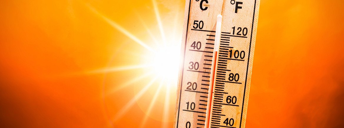 Wooden thermometer showing near-maximum temperature against a bright orange sun.