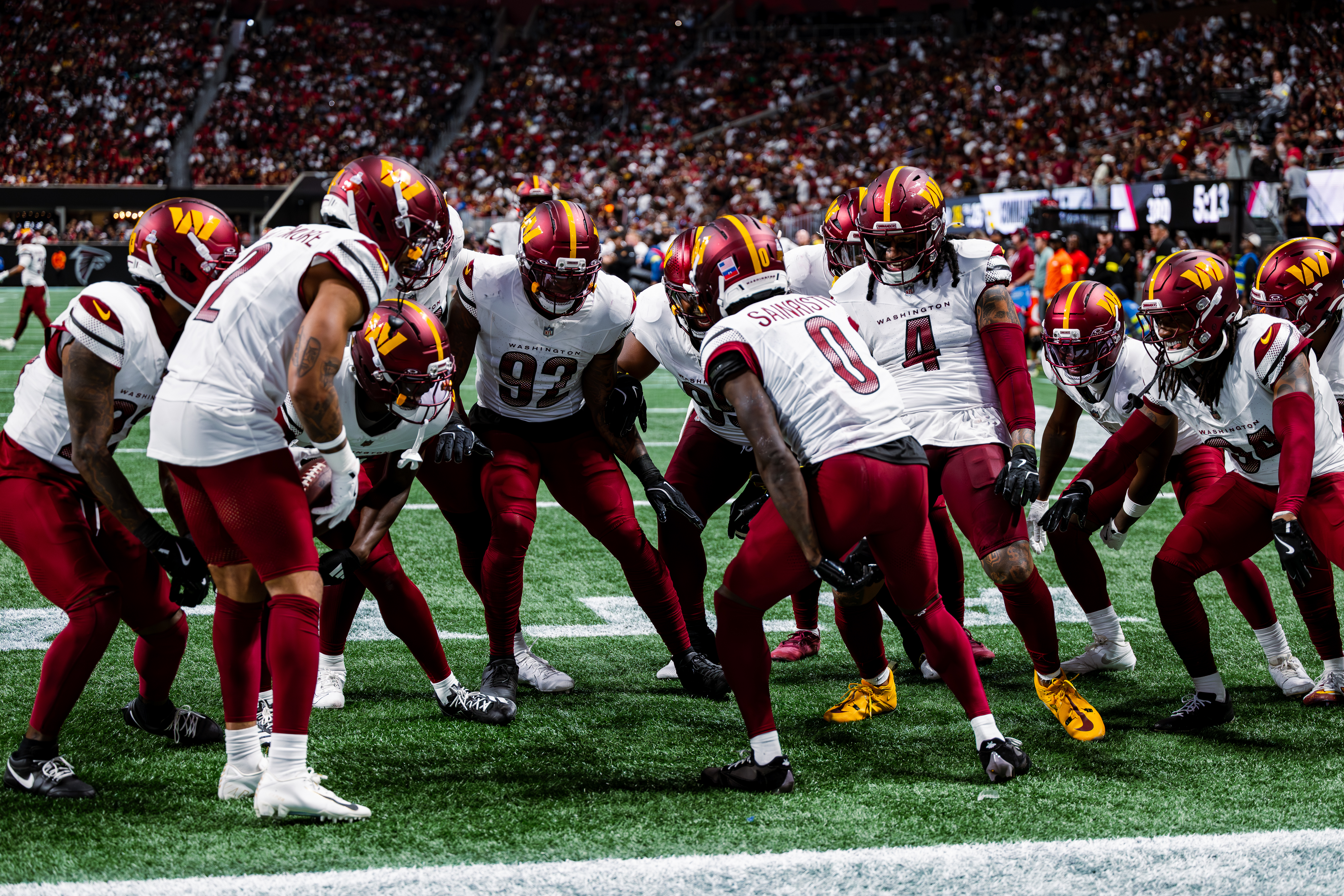 Washington Commanders players in white jerseys line up in formation on a football field before a packed stadium.