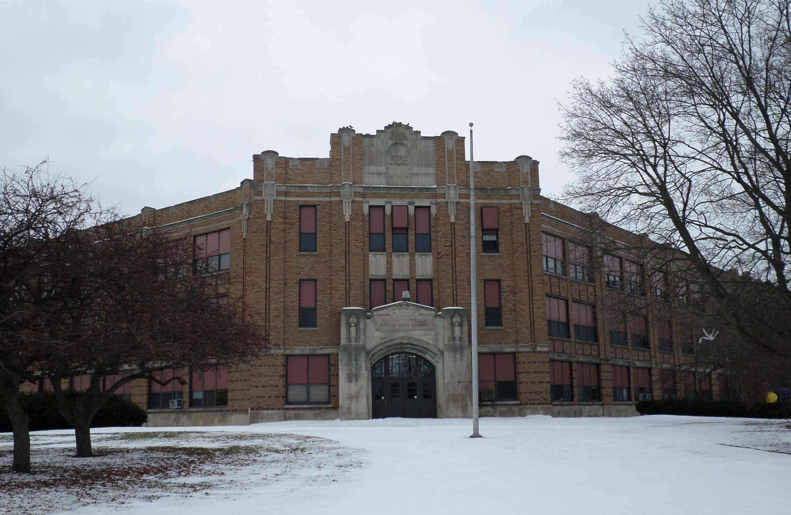 Three-story brick school building with arched entrance surrounded by snow-covered grounds and bare trees.