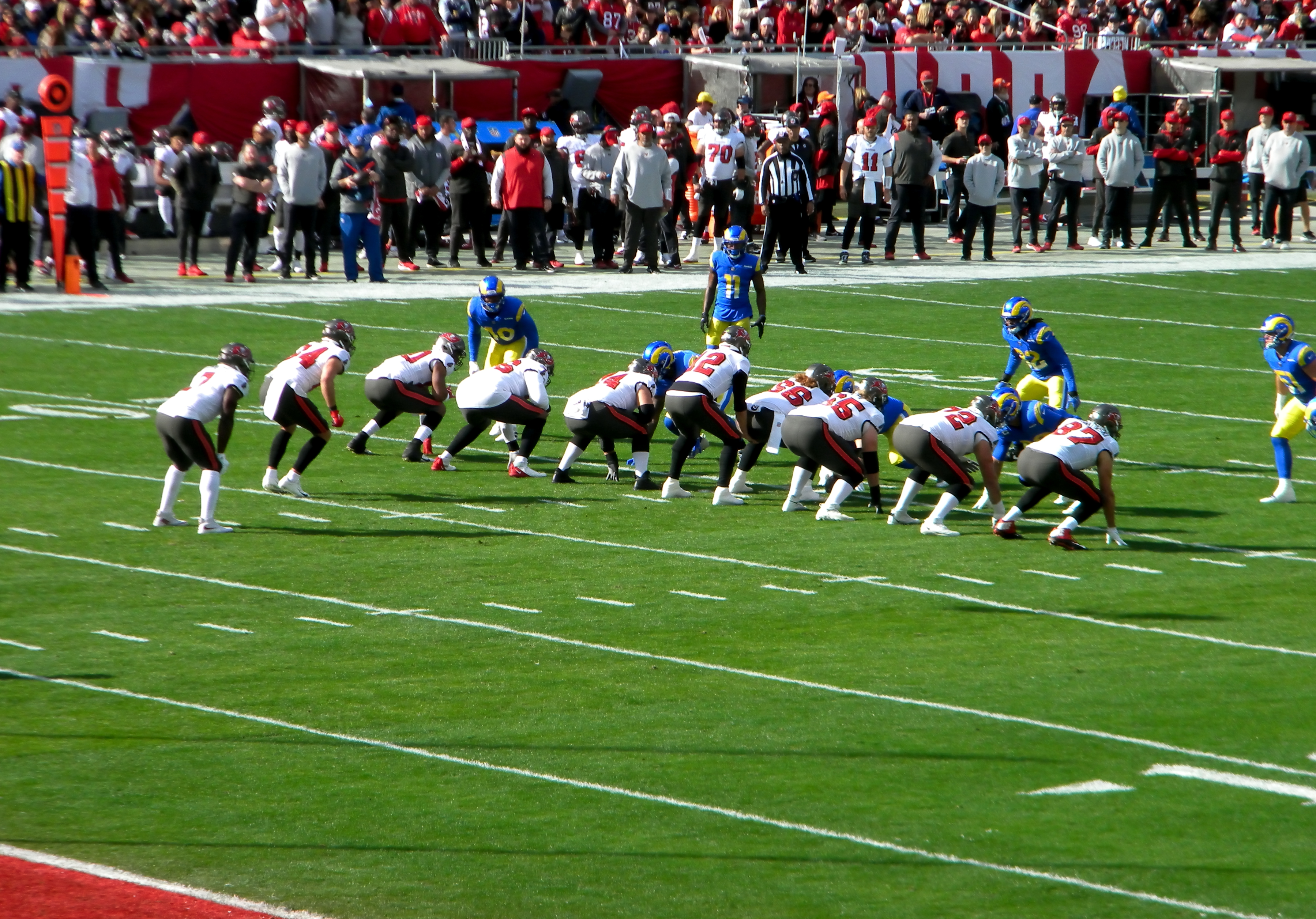 NFL players in red and blue uniforms lined up at the line of scrimmage on a grass field.