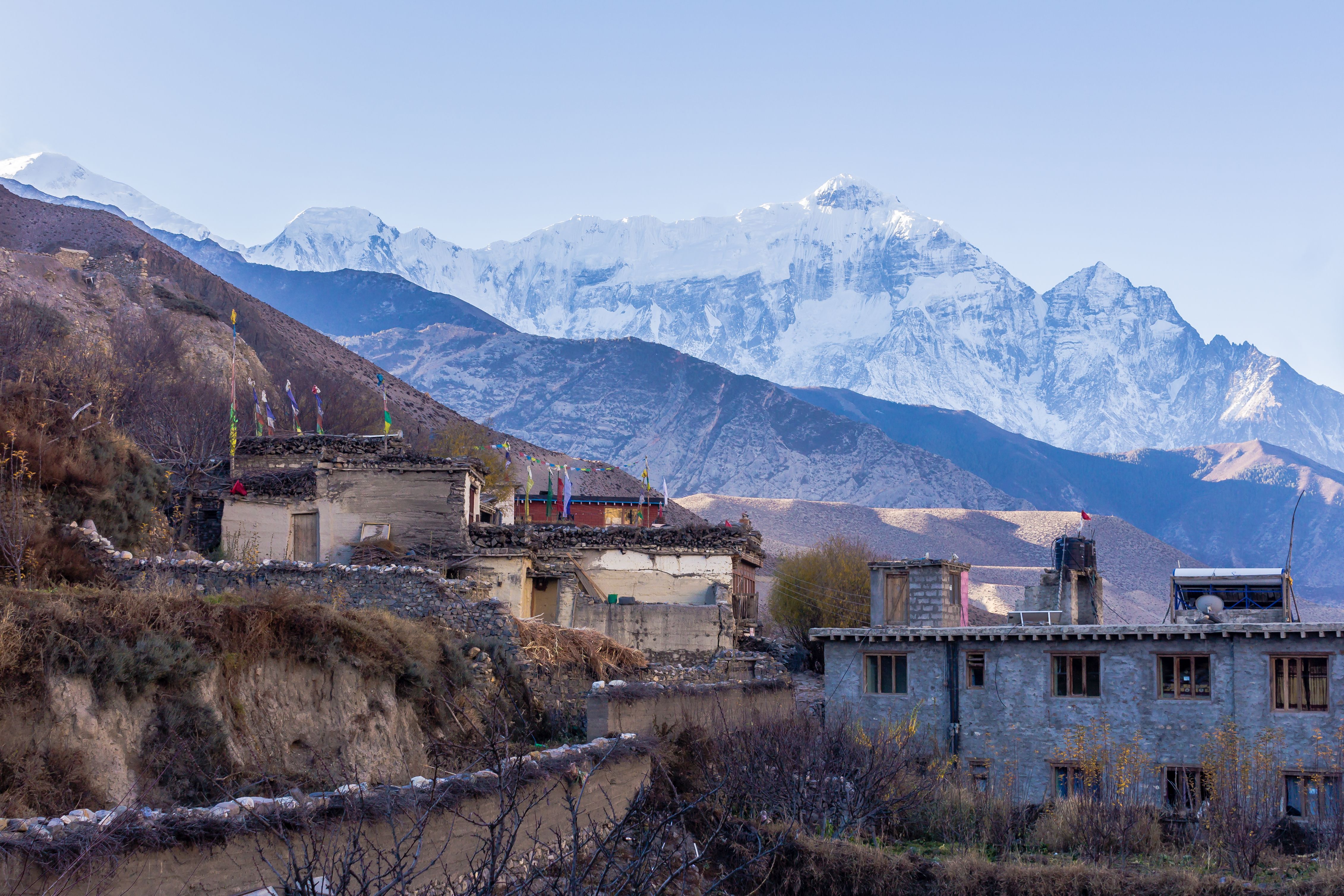 Traditional stone buildings of a Himalayan village with snow-capped mountain peaks behind.